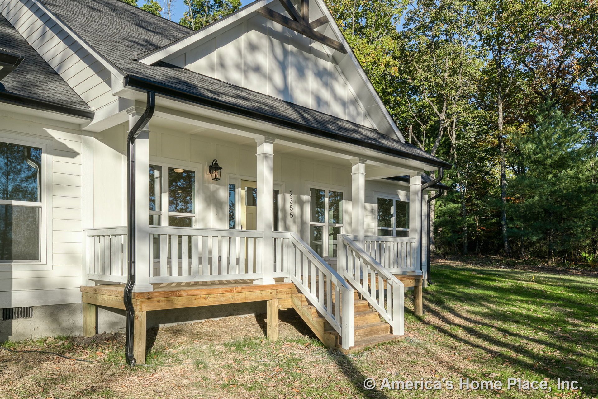 Covered front porch with white railings and columns, wooden steps, white horizontal siding, black shingle roof, multiple front windows, decorative gable trim, exterior wall