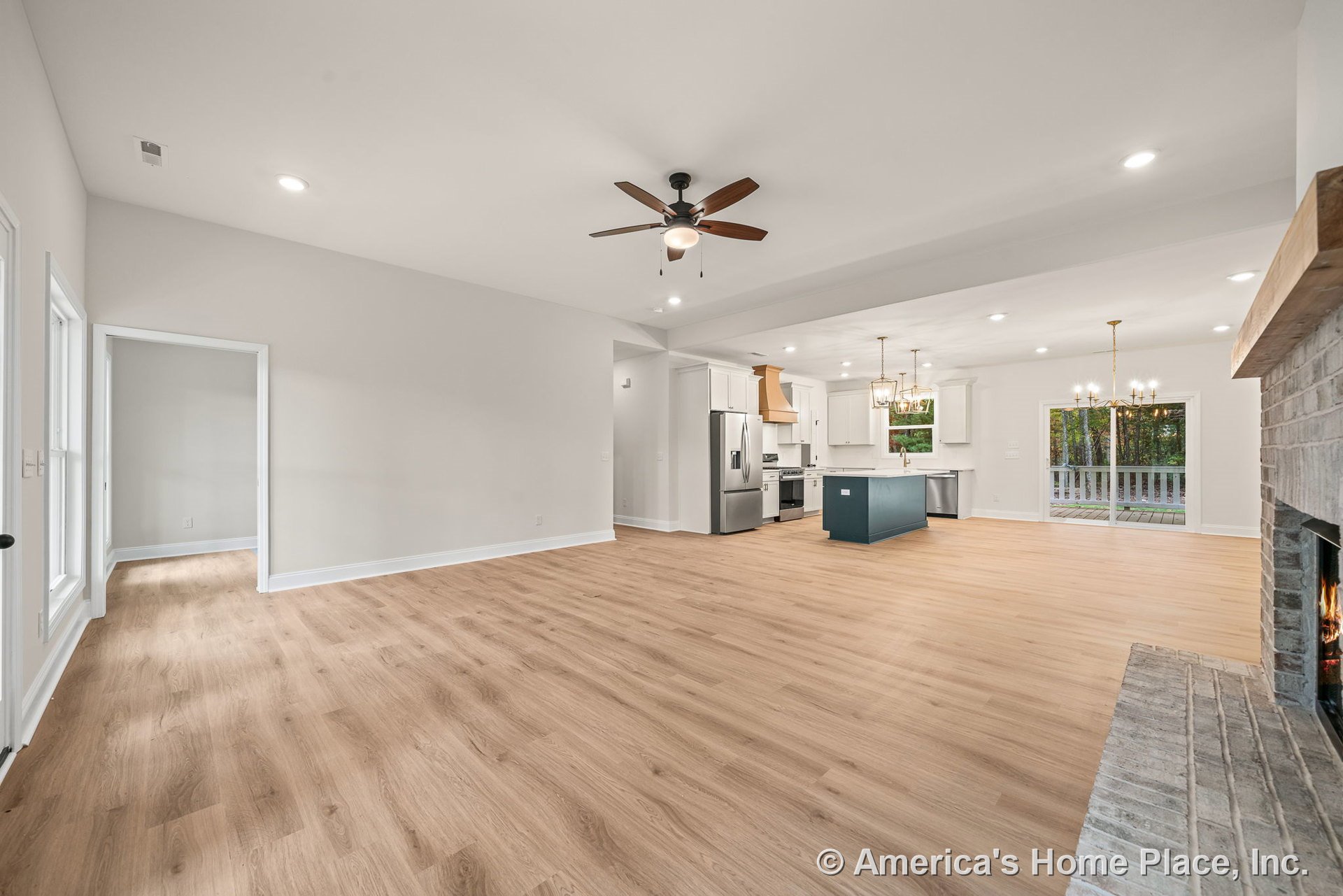 Open concept living area with light wood plank flooring, brick fireplace with wood mantel, modern kitchen featuring white cabinetry, blue island, stainless appliances, recessed