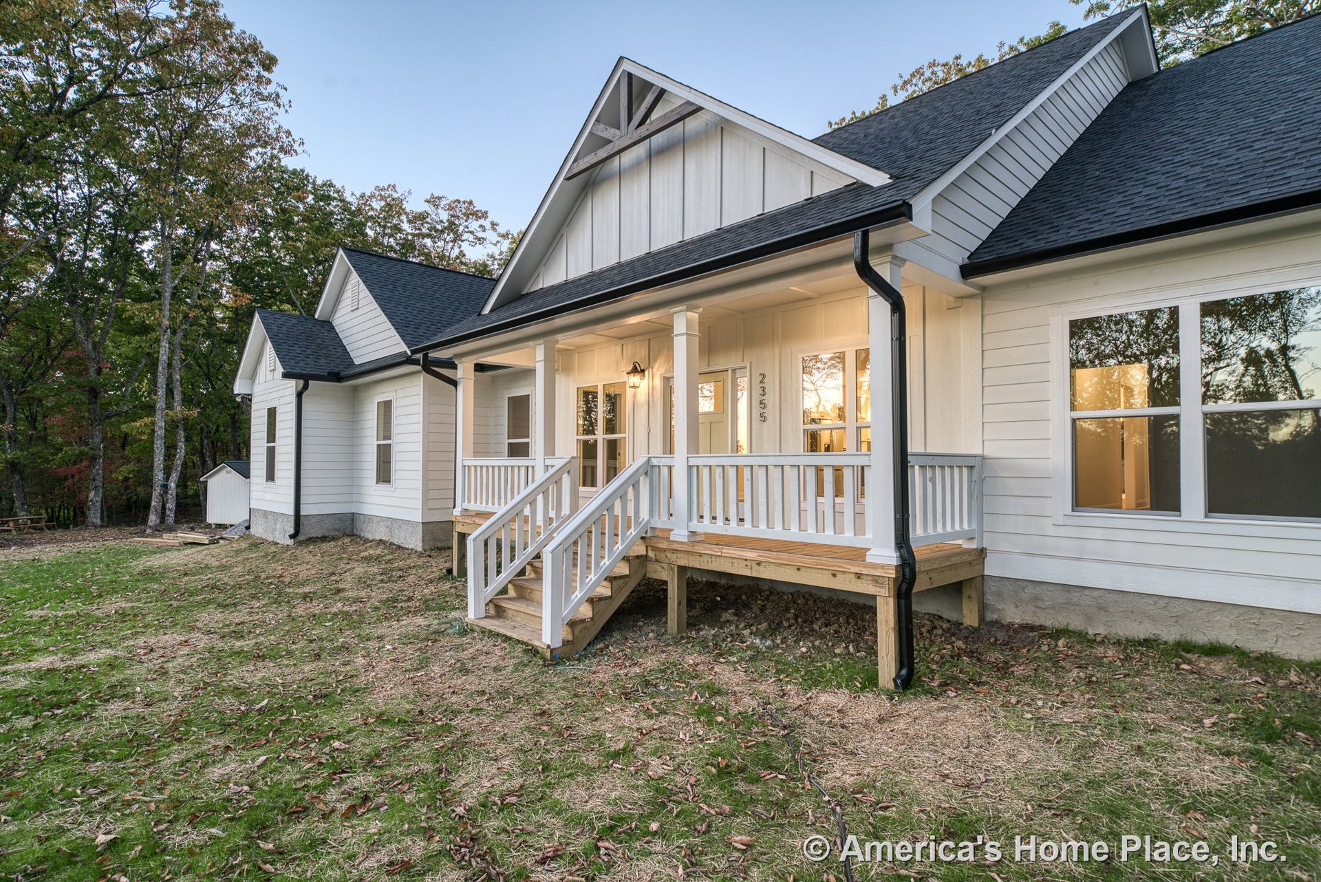 White board-and-batten siding with black roof shingles, covered front porch supported by columns, wood steps leading to double front doors with glass panels, exterior wall-mounted