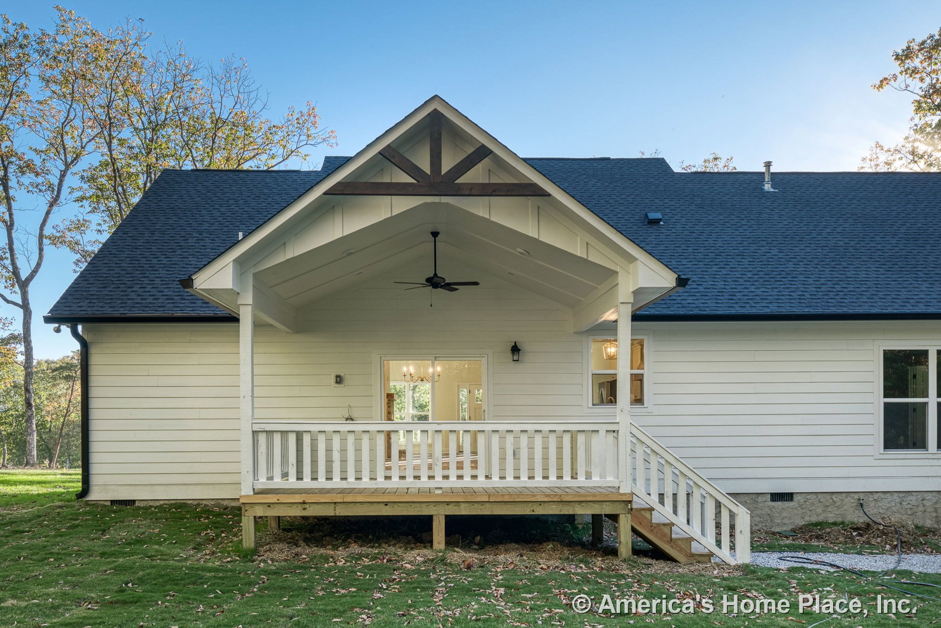 Covered rear porch with white railing, gabled roof featuring exposed wood beams, white horizontal siding, wooden porch steps, ceiling fan, double glass doors, exterior lighting