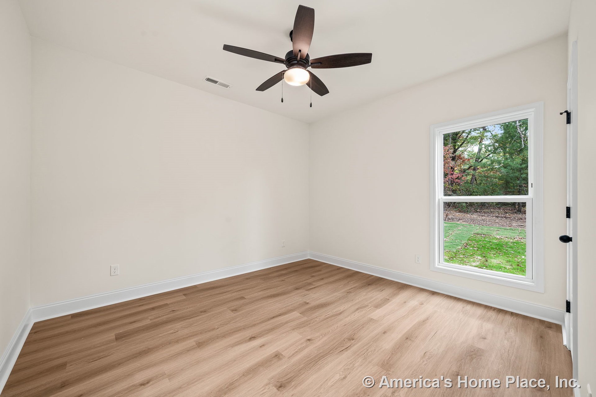 Light wood plank flooring with white baseboard trim, large single window allowing natural light, dark ceiling fan with built-in lighting, neutral wall color, ceiling vent, and door