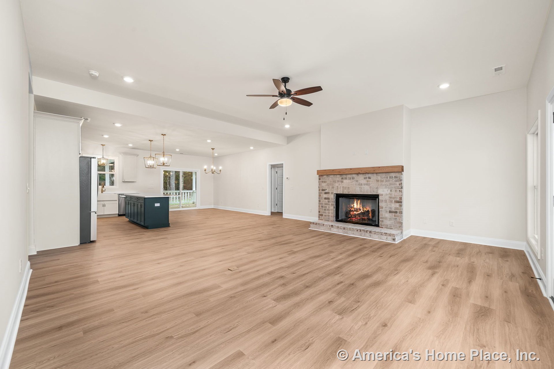 Open floor plan with brick fireplace and wood mantel, light wood plank flooring, kitchen featuring white cabinetry and dark blue central island, recessed ceiling lights, large