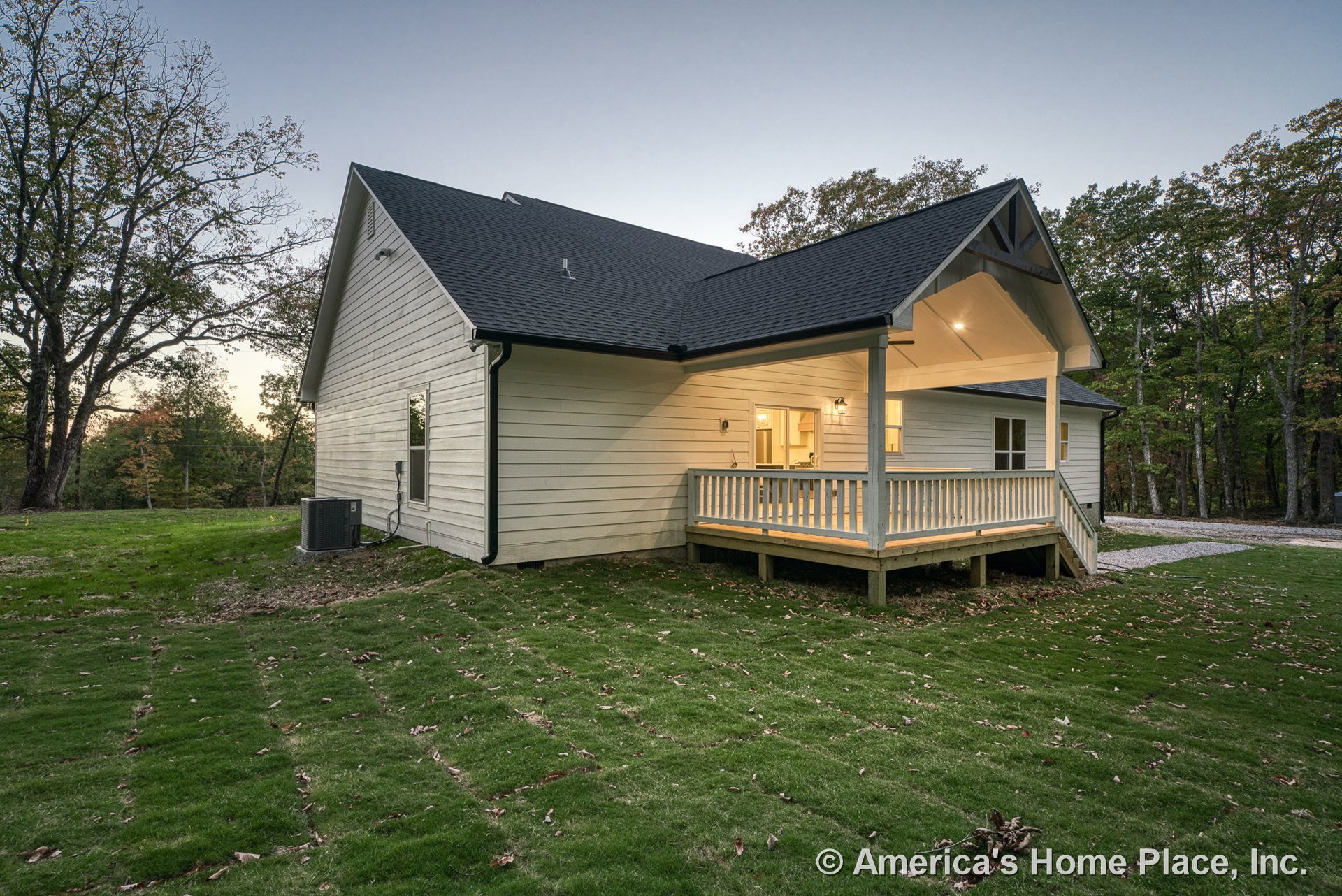 Covered back porch with wood railings and steps, gabled roof, horizontal siding, exterior lighting fixtures, windows with trim, and freshly laid sod lawn in a rural backyard