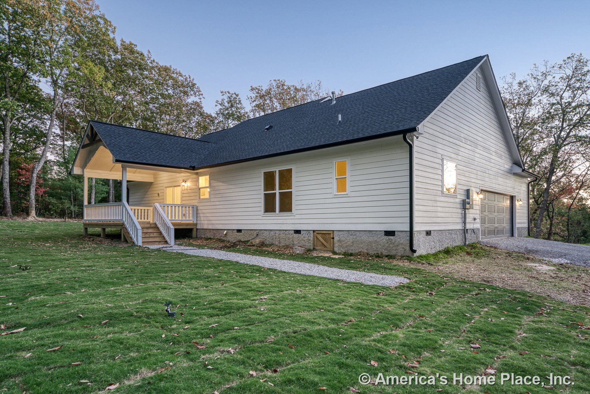 White horizontal siding exterior with covered front porch featuring railing and steps, attached two-car garage with paneled doors, black shingle roof, double-hung windows, exterior