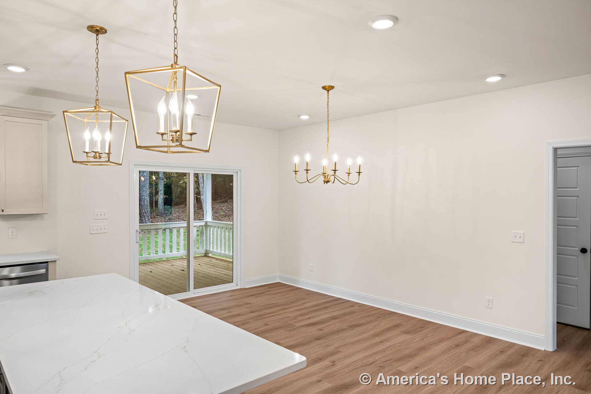 Gold chandelier hangs above dining area with light wood plank flooring, sliding glass door opens to covered porch with railing, white quartz countertop and recessed ceiling lights