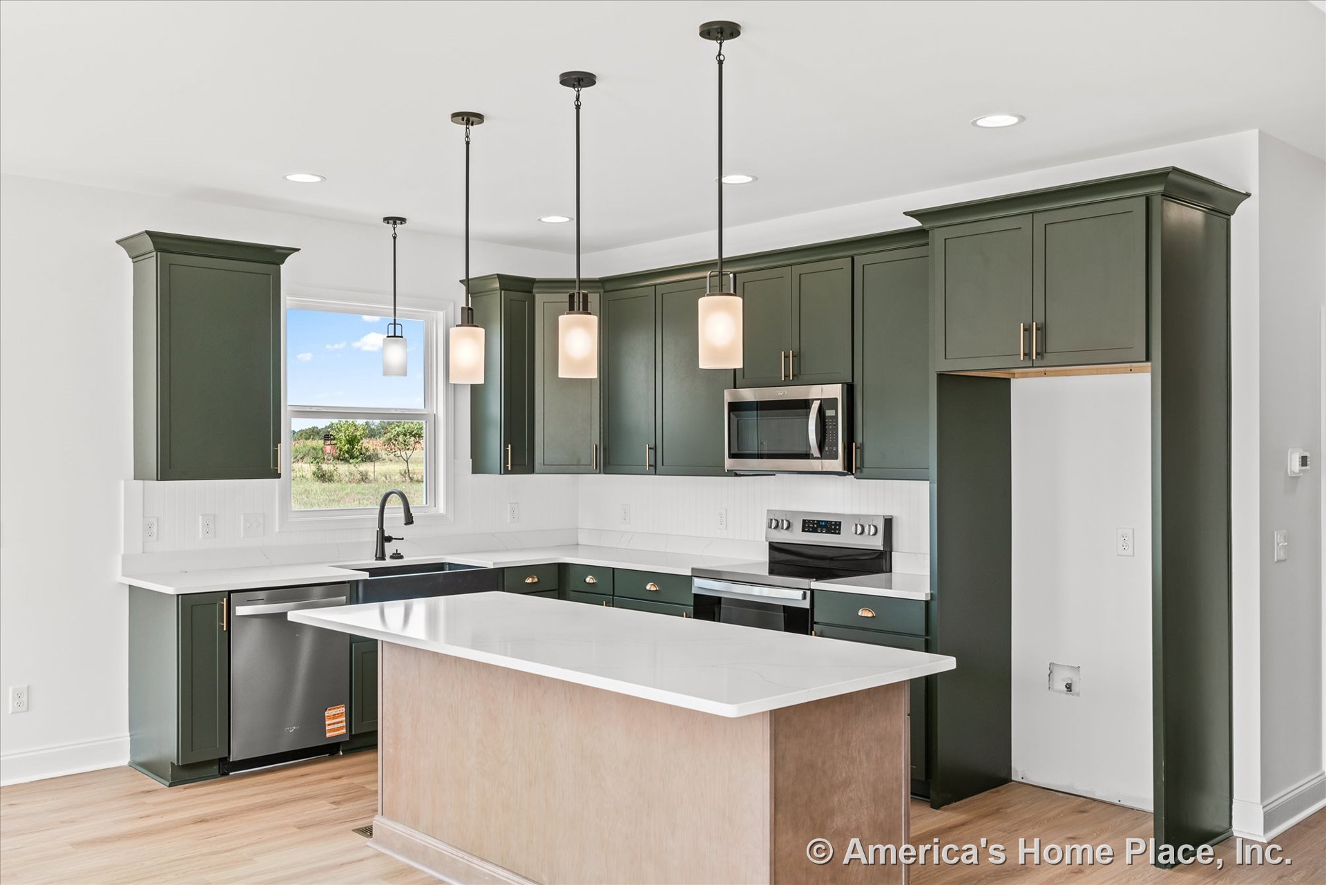 Green shaker cabinets with brushed hardware, white quartz countertops, three pendant lights above a central island, stainless steel appliances including built-in microwave, large