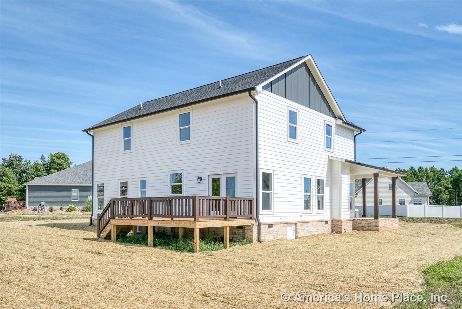 White horizontal siding exterior with multiple rectangular windows, covered porch supported by columns, raised wooden deck at the rear, brick foundation, dark shingle roof