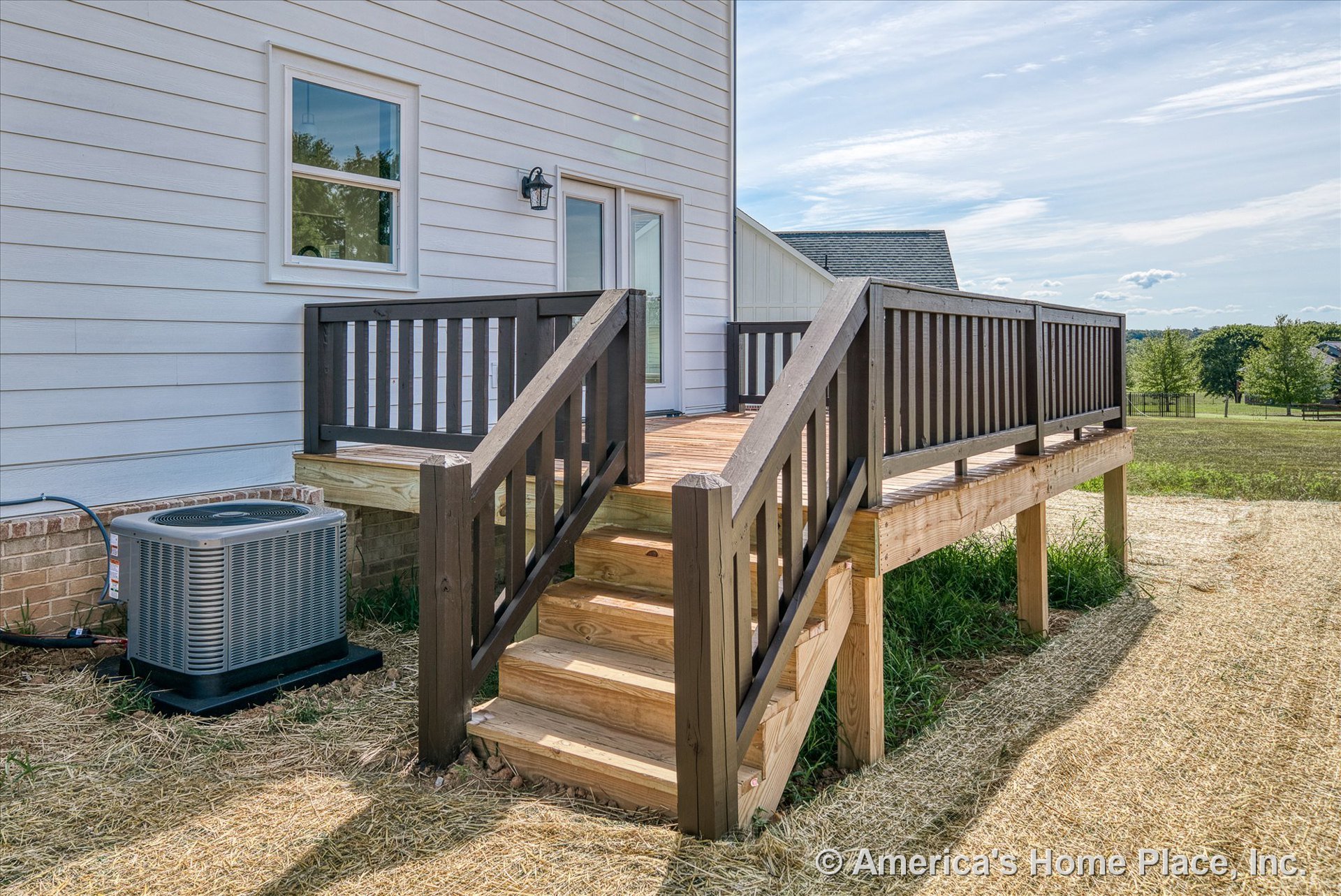 Elevated wooden deck with matching stairs and dark wood railings, attached to white horizontal siding exterior featuring a window, door, and outdoor wall light fixture.