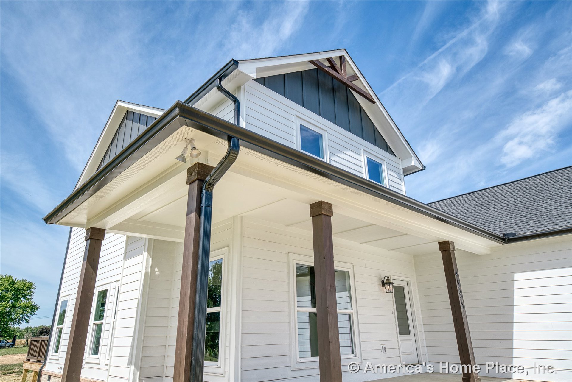 White horizontal siding with contrasting dark trim, covered front porch supported by dark wood columns, double-hung windows, exterior lighting fixture beside entry door, gable roof