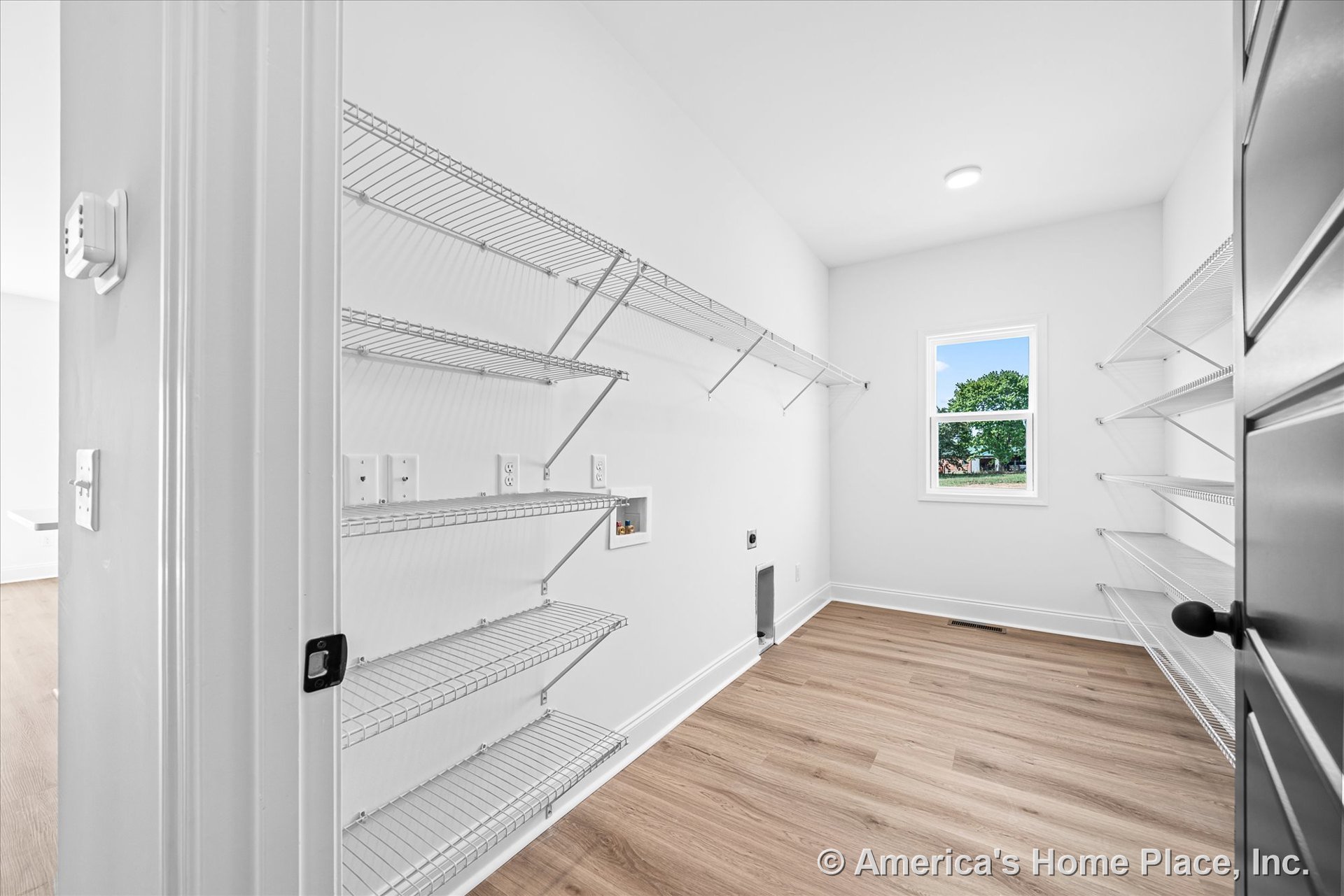 Laundry room with wire shelving on both walls, utility hookups for washer and dryer, single window with white trim, light wood-look flooring, recessed ceiling light, white painted