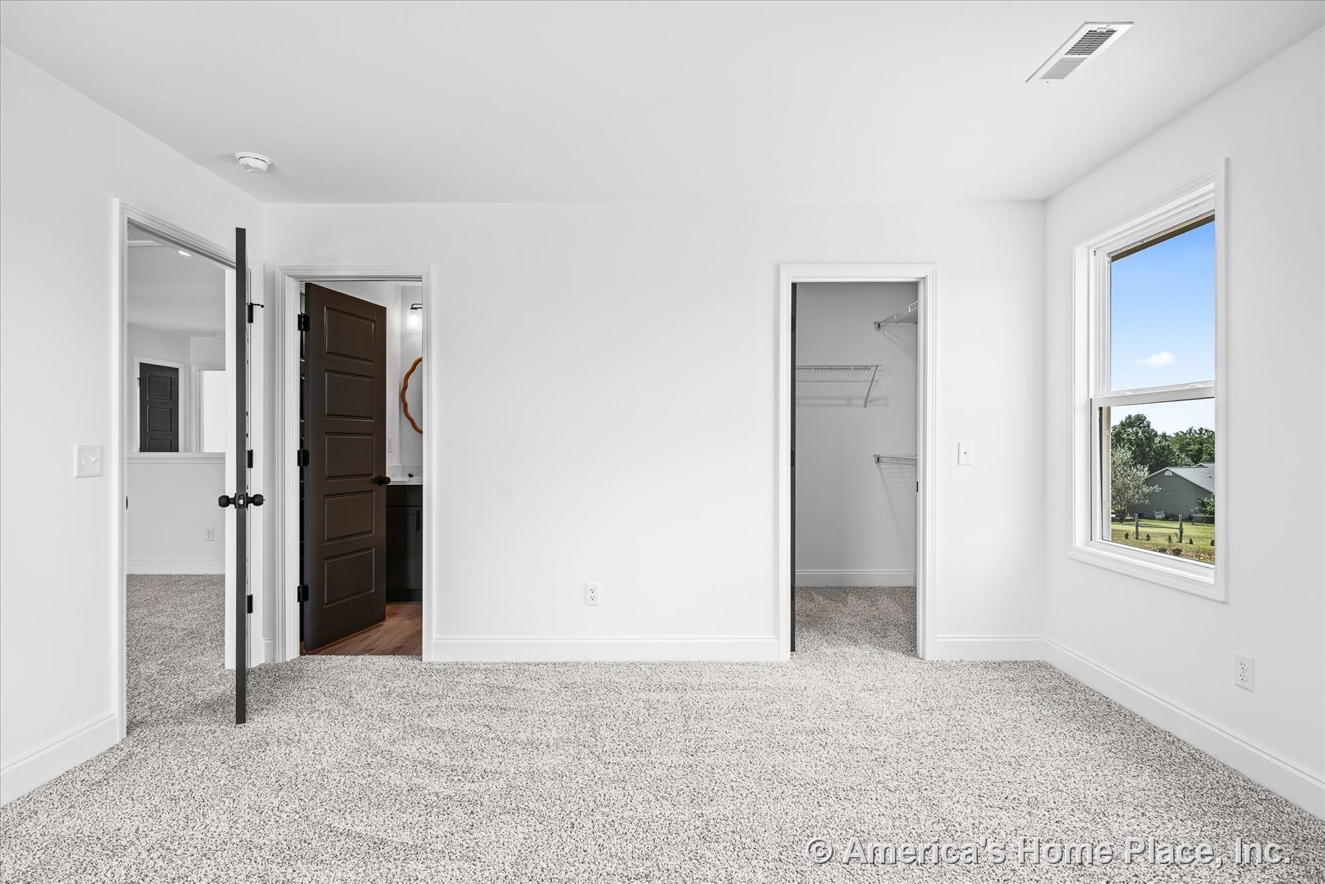 Bedroom with light carpet flooring, white painted walls, walk-in closet featuring wire shelving, large window framed by white trim, dark paneled interior doors, ceiling vent, and