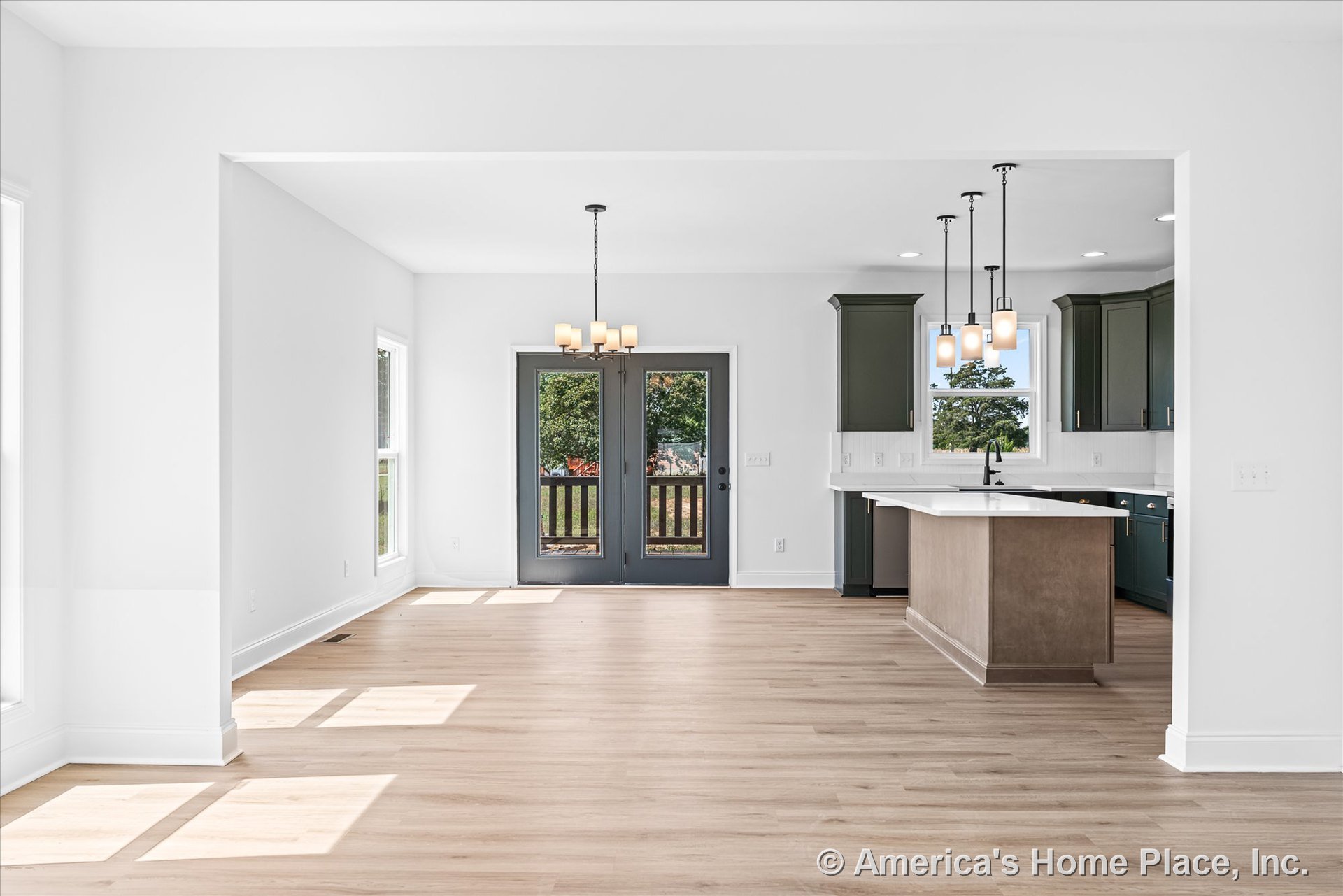 Open kitchen and dining area with light wood flooring, double glass doors with white trim, large windows with white frames, kitchen island featuring a white countertop, dark green