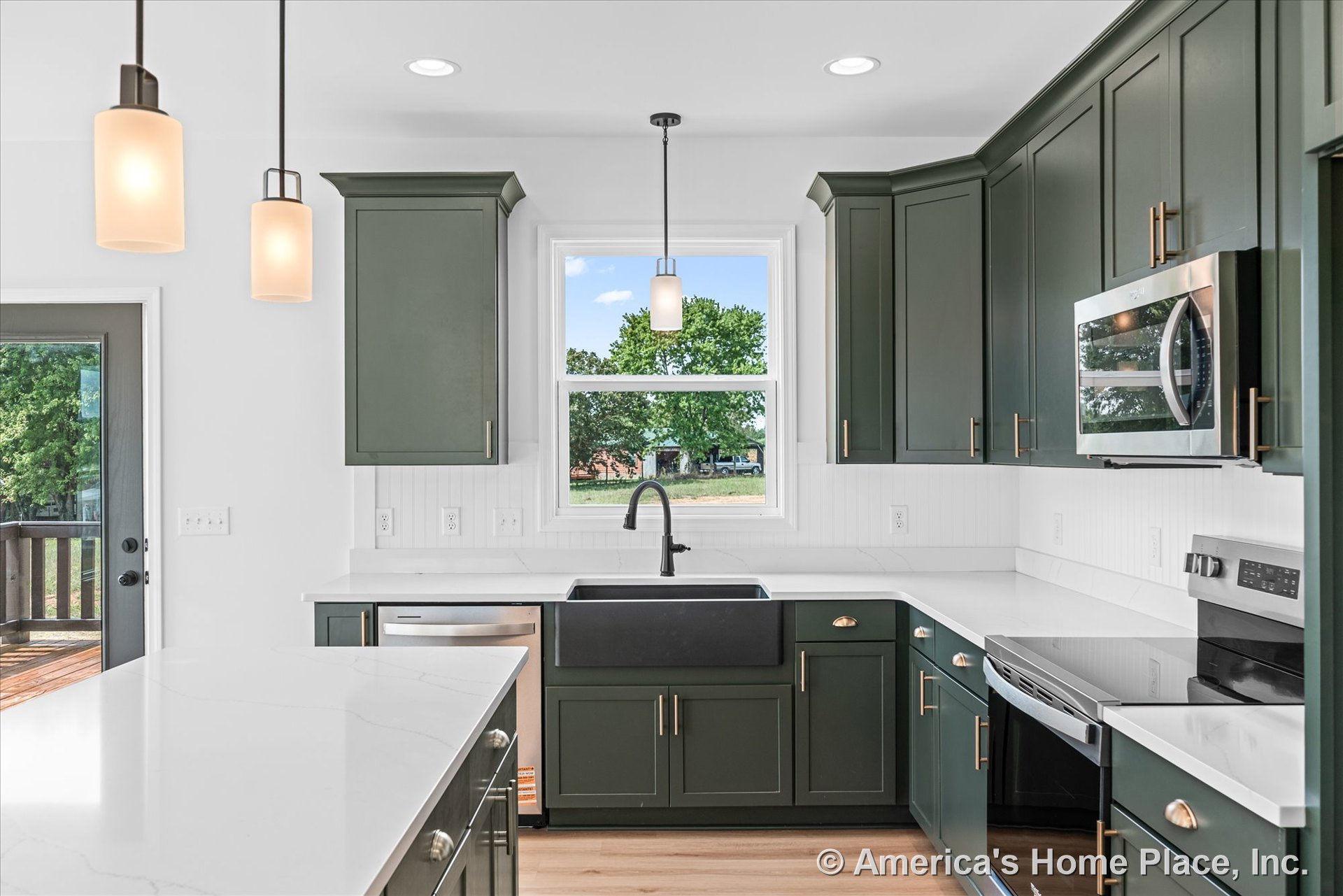 Green shaker cabinets with white quartz countertops, black farmhouse sink under a large window, stainless steel appliances, beadboard backsplash, pendant and recessed lighting