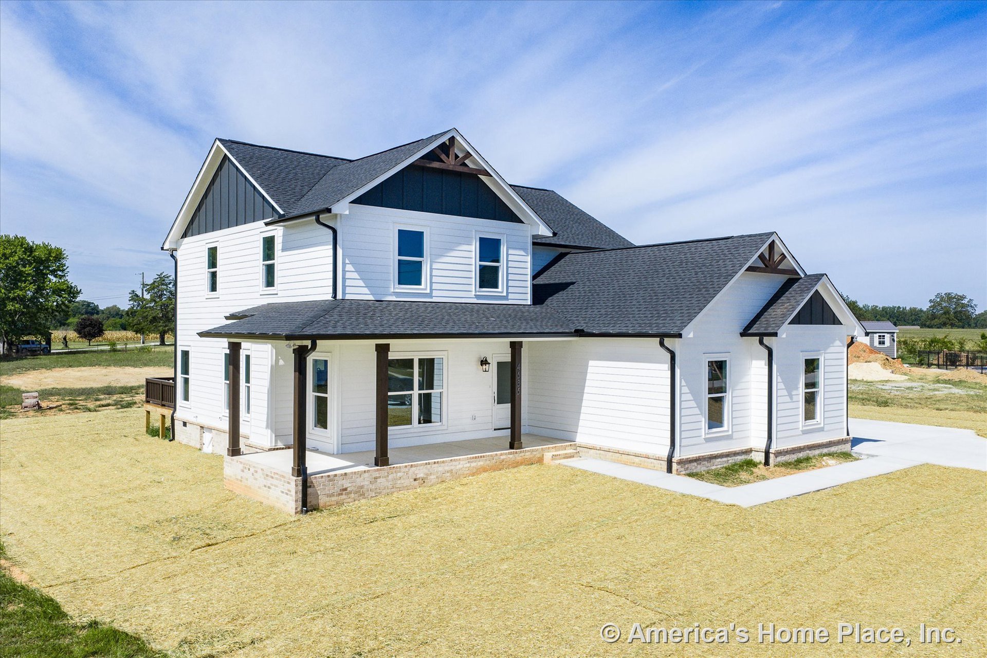 Two-story home with white horizontal siding, black architectural roof shingles, covered front porch trimmed in brick, and multiple double-hung windows with black accents.