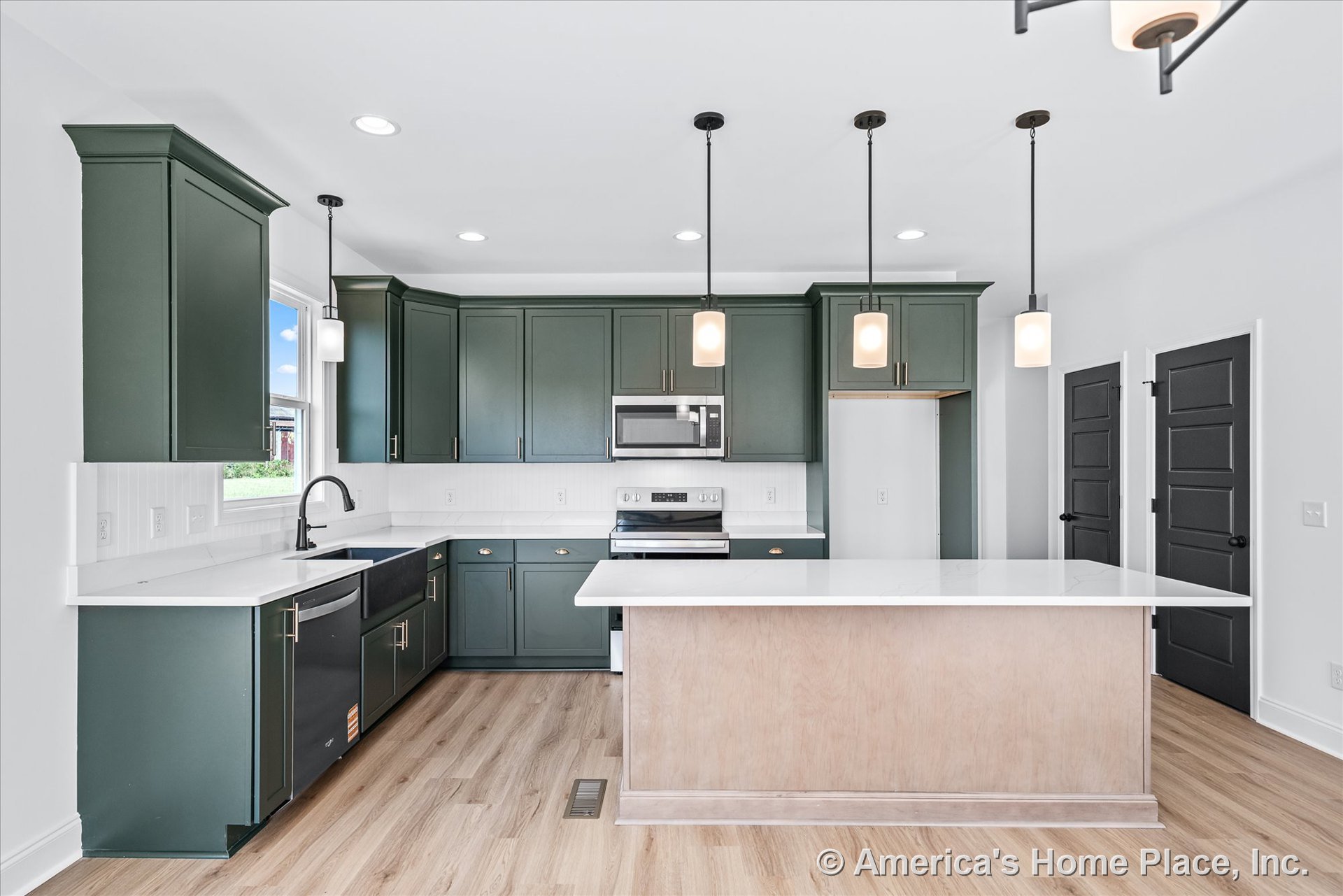 Green shaker cabinets with white quartz countertops, stainless steel appliances, farmhouse sink beneath window, pendant lights above light wood island, white backsplash, built-in