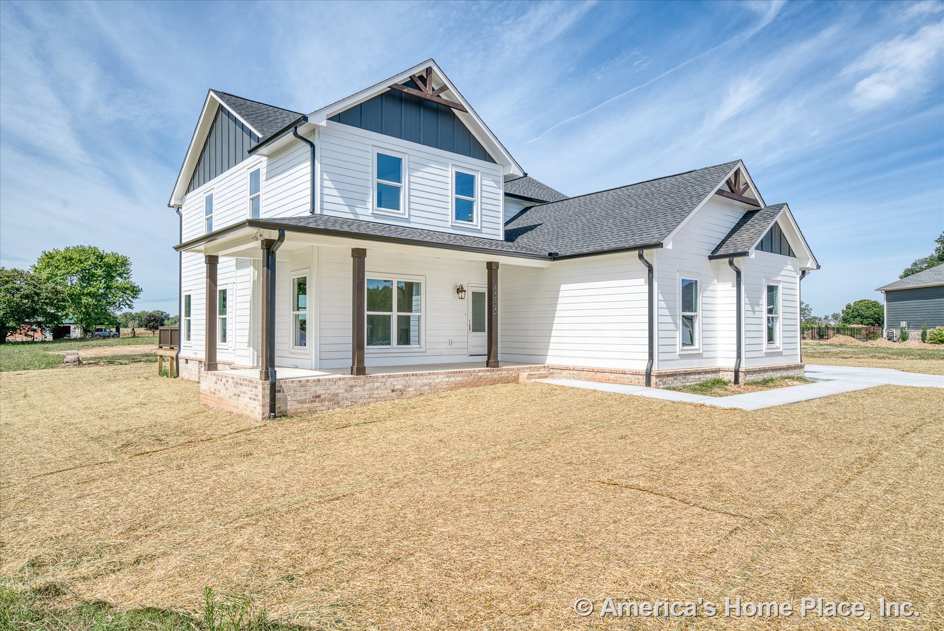 White horizontal siding with brick foundation trim, covered front porch supported by wood columns, multiple double-hung windows, dark shingle roof, permanent lighting along trim.