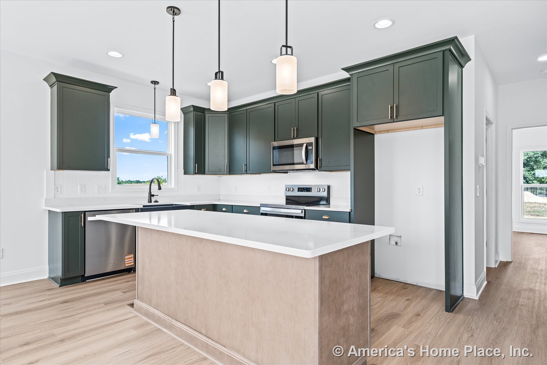 Dark green upper and lower kitchen cabinets with white quartz countertops, central island beneath pendant lights, stainless steel appliances, tile backsplash, built-in microwave