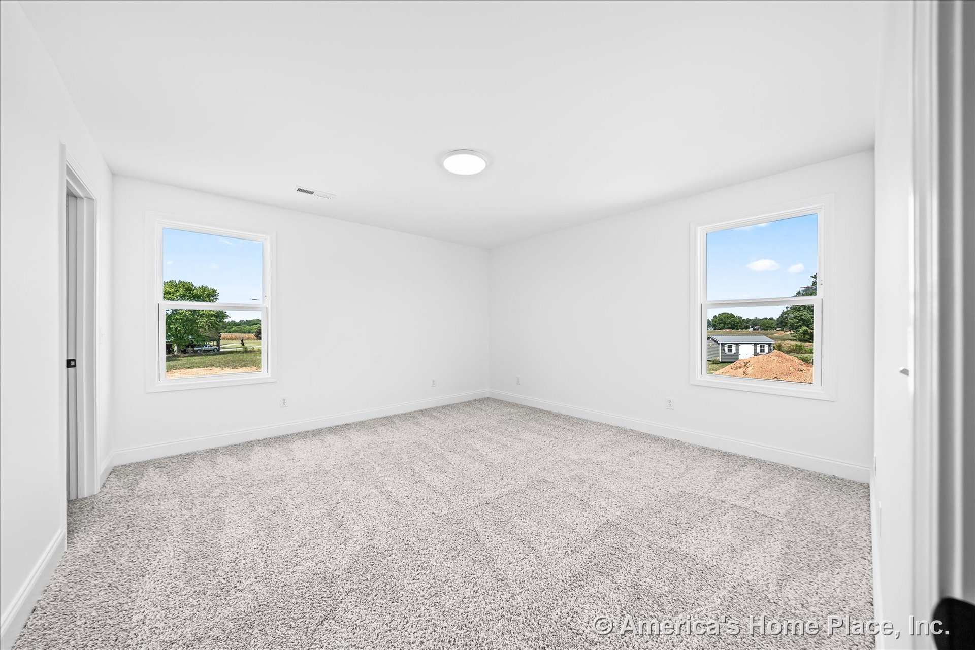 Bedroom with neutral carpet flooring, double window layout, smooth white walls, white trim and baseboards, flush mount ceiling light, and doorway to adjacent room.