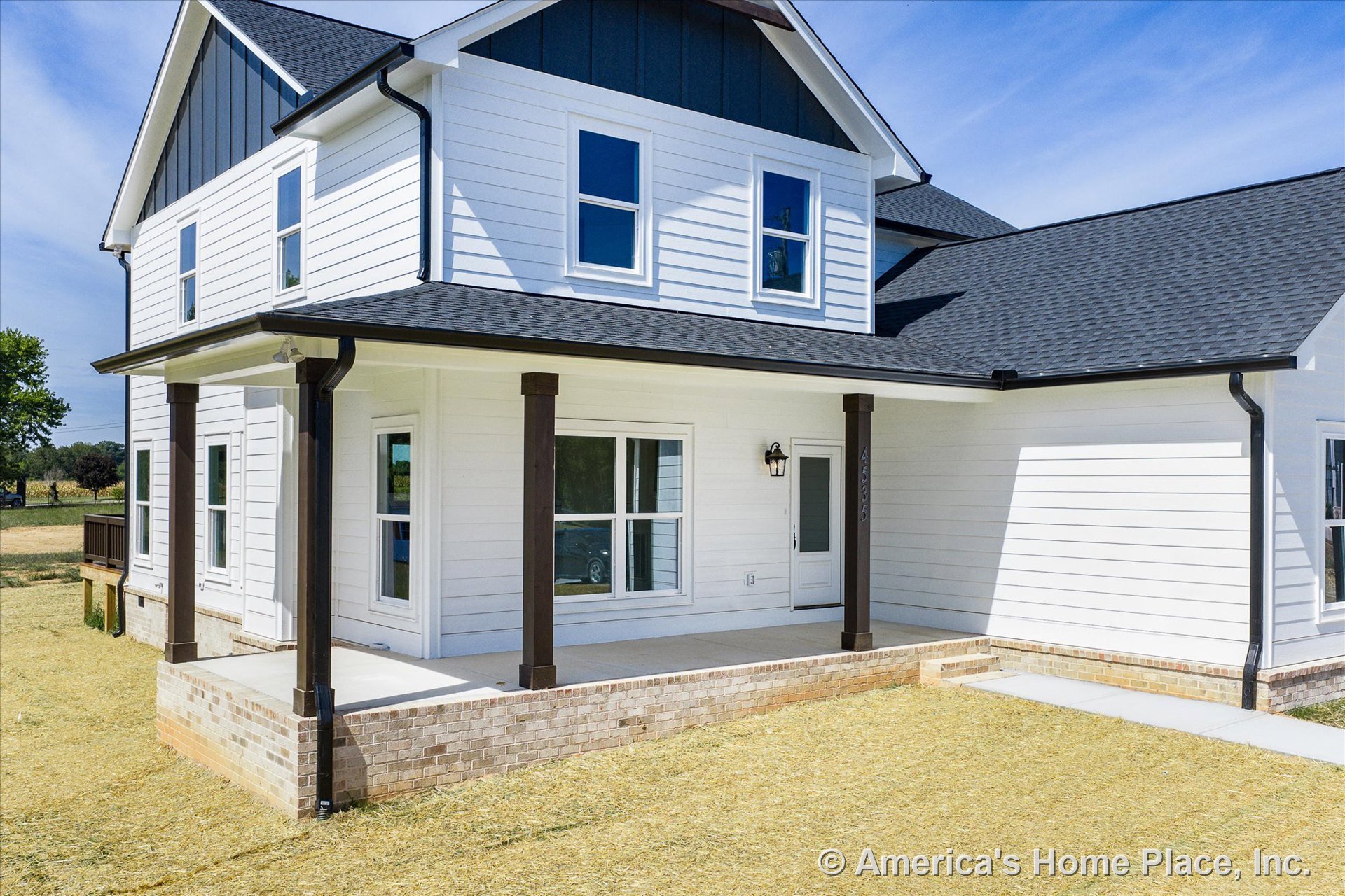 White horizontal siding with dark trim, covered front porch supported by dark wood columns, brick skirting along porch base, double-hung windows, dark roof shingles, exterior