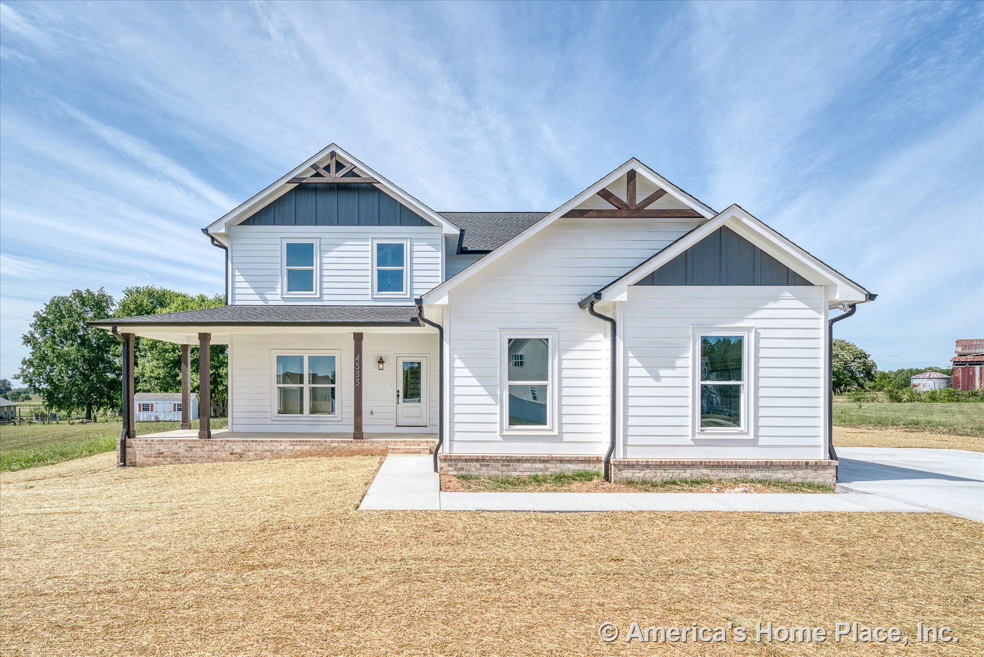 White horizontal siding and brick foundation trim on a two-story farmhouse-style home with decorative gable brackets, covered front porch, double-hung windows, entry door, and