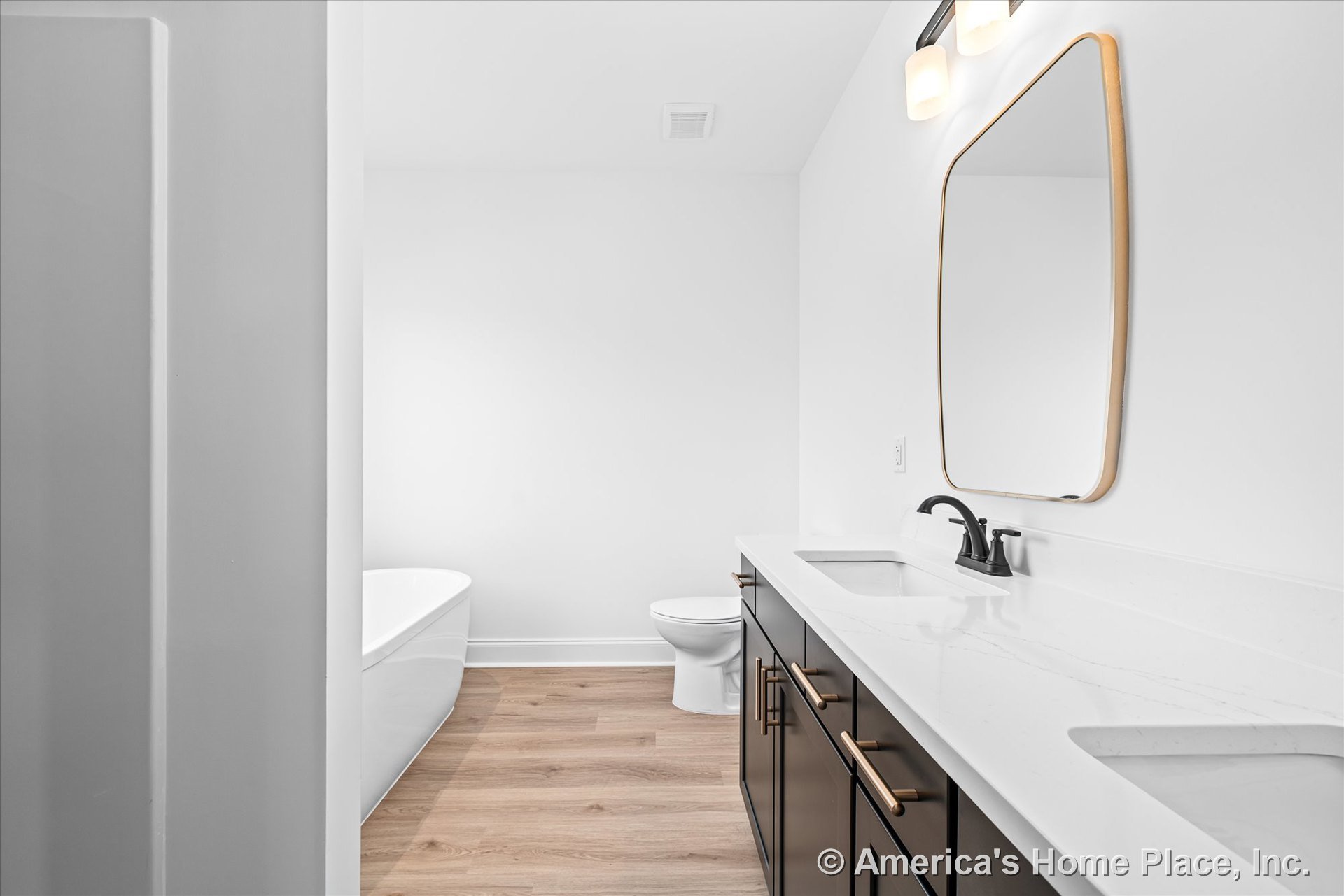 Double vanity with quartz countertops and matte black faucets, freestanding bathtub, wood-look flooring, wall-mounted lighting fixtures, large mirrors, white walls, modern