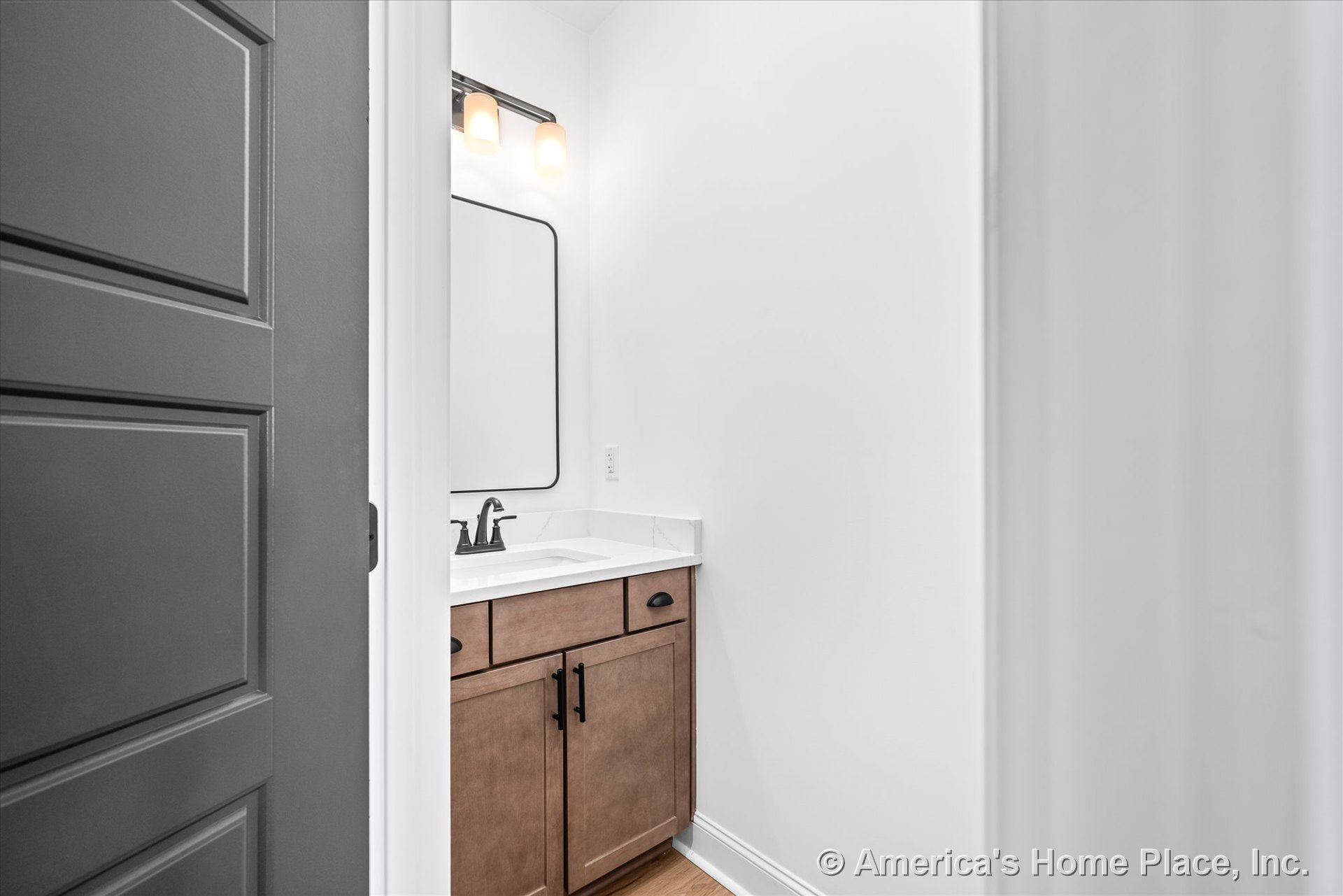 Wood vanity cabinetry with white quartz countertop, black faucet and hardware, rectangular black framed mirror, wall-mounted light fixture, white walls and trim.