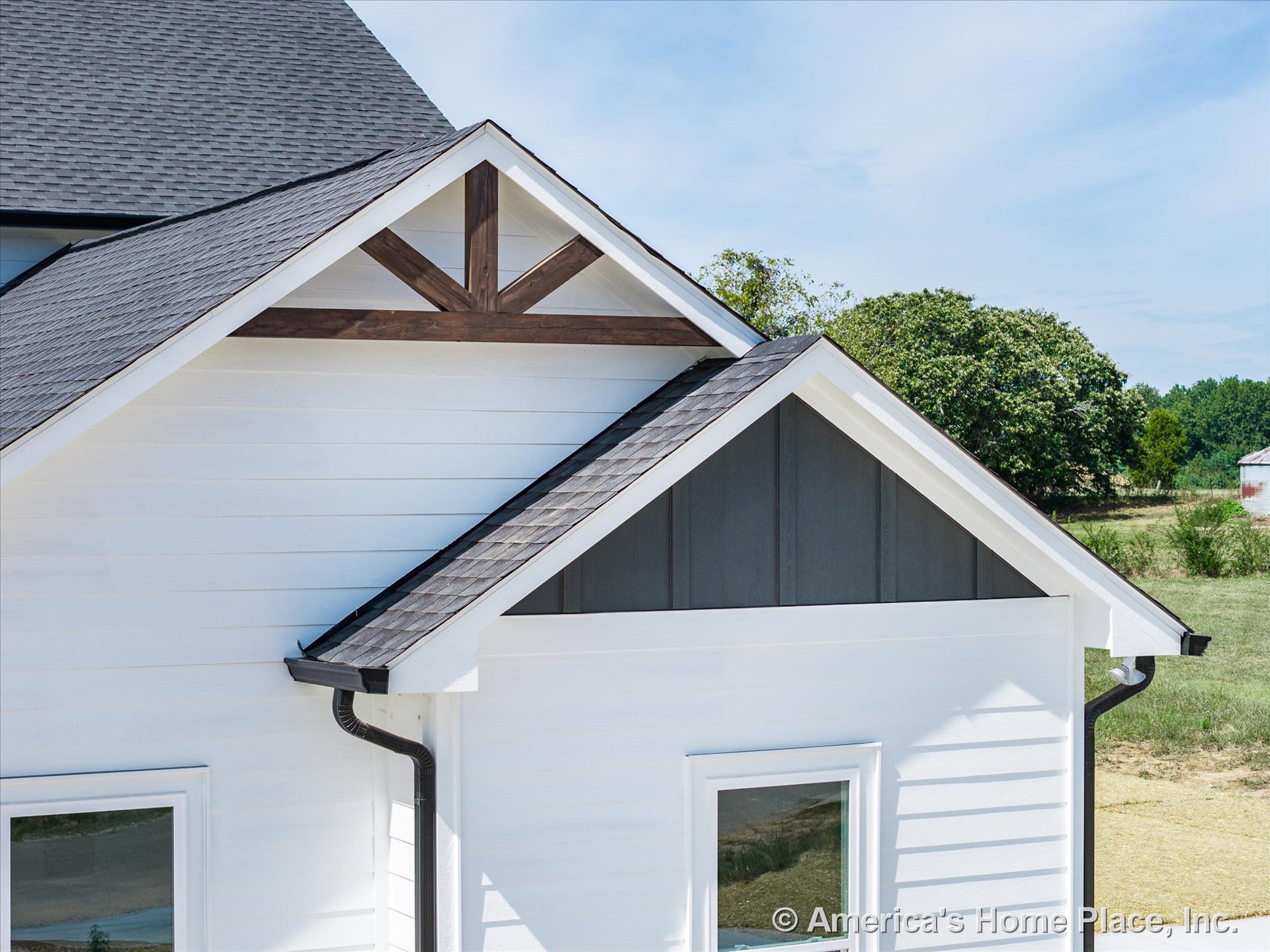 White horizontal siding paired with dark vertical gable panels, decorative wood trim in gables, asphalt shingle roof, white-framed windows, and black gutter system.