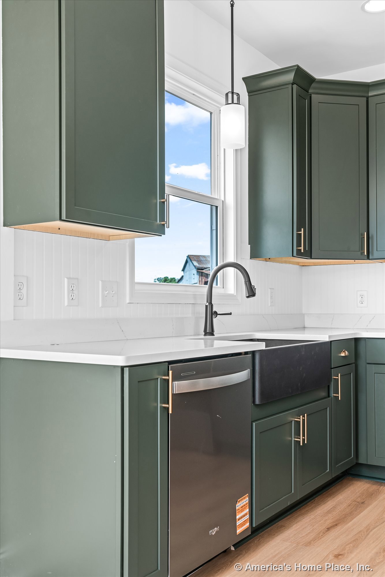 Green shaker cabinets with brass hardware, white quartz countertops, black farmhouse sink set beneath a window, white tile backsplash, pendant light fixture, built-in dishwasher