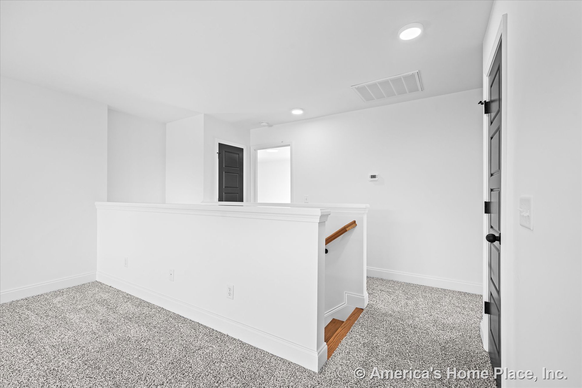 Upstairs landing with carpet flooring, white painted trim and baseboards, recessed ceiling lights, dark paneled doors, wood stair railing, wall-mounted thermostat, and painted