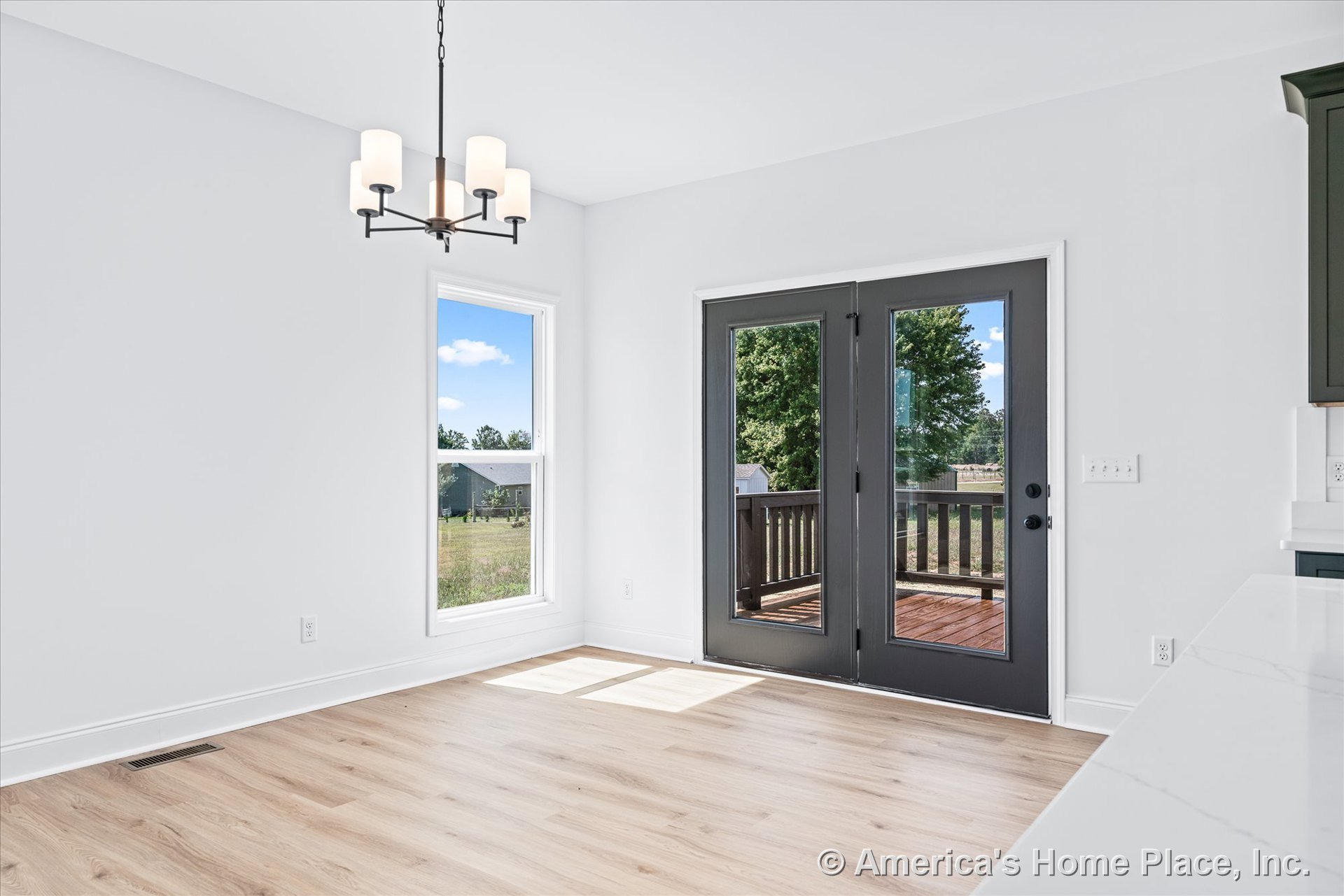 Dining area with light wood plank flooring, white walls and trim, black framed double glass doors opening to a covered porch, single large window, and a modern chandelier providing