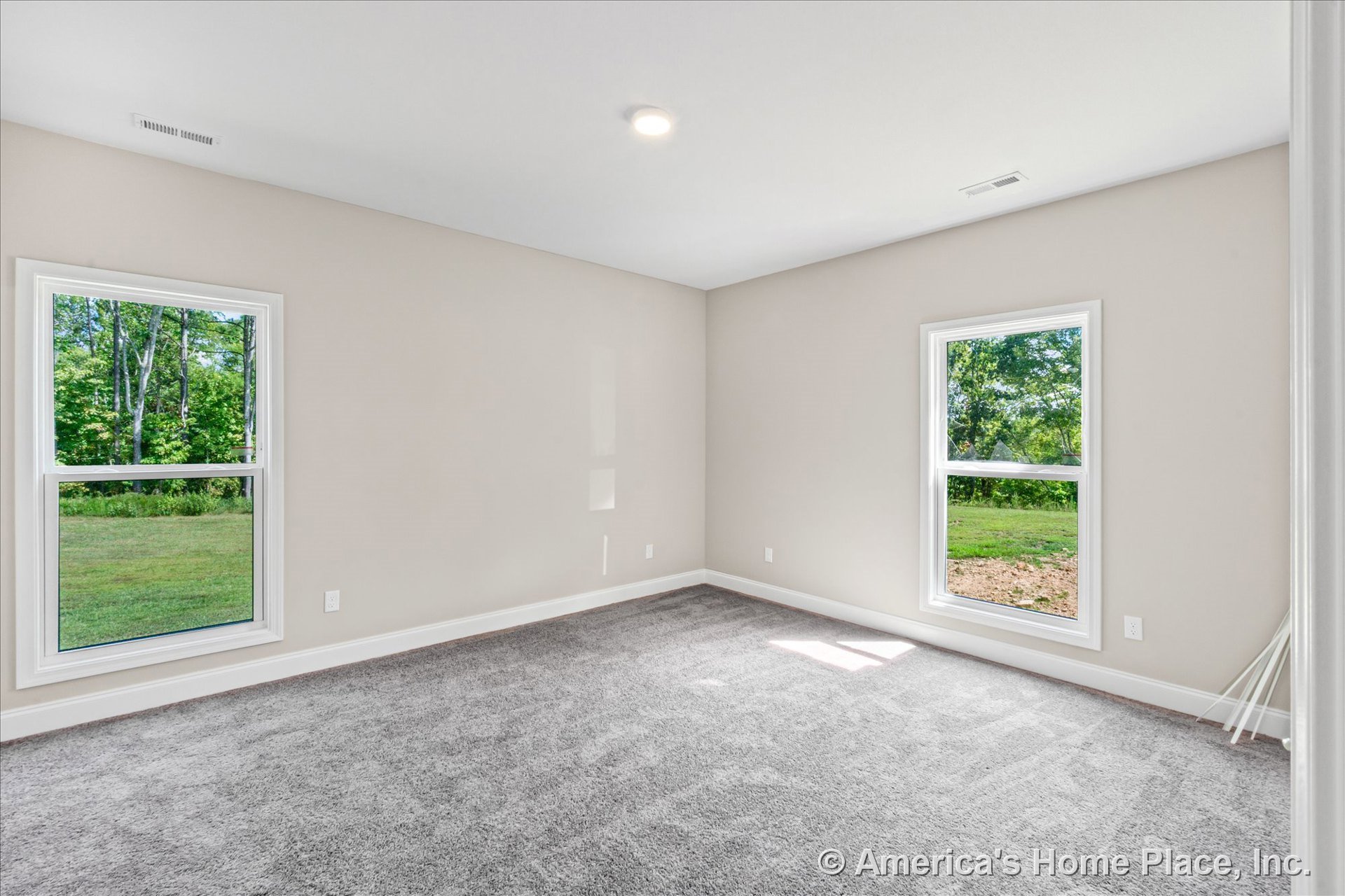 Bedroom with two large double-hung windows, light gray carpet flooring, beige painted walls, white baseboard trim, and recessed ceiling light in an empty new construction interior.