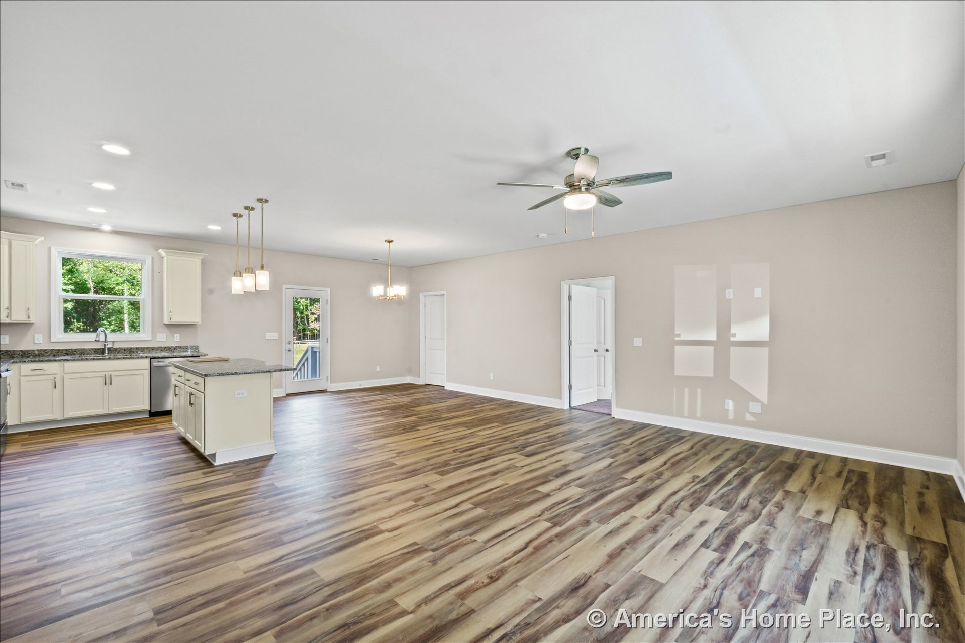 Open-concept kitchen and living area with wood-look plank flooring, granite countertops, kitchen island, white cabinetry, ceiling fan with light, multiple pendant lights above