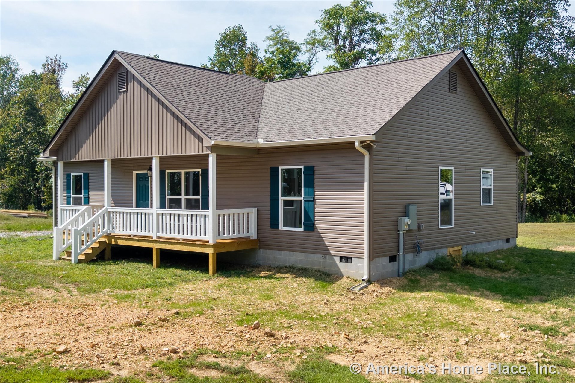 Tan vinyl siding exterior with gable roof clad in asphalt shingles, covered front porch featuring white railings and steps, blue window shutters, visible exterior utility box and