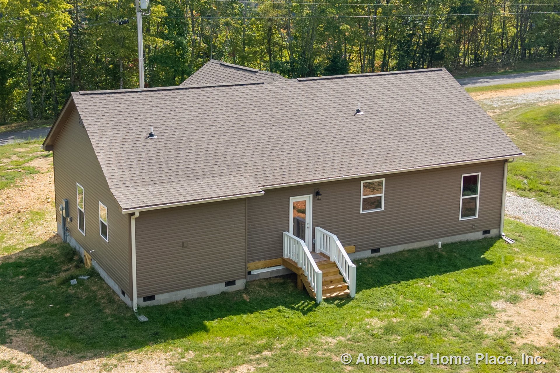 Brown vinyl siding exterior with shingle roof, small entry porch featuring white railings and steps, rectangular windows, single exterior door, white trim, and outdoor lighting