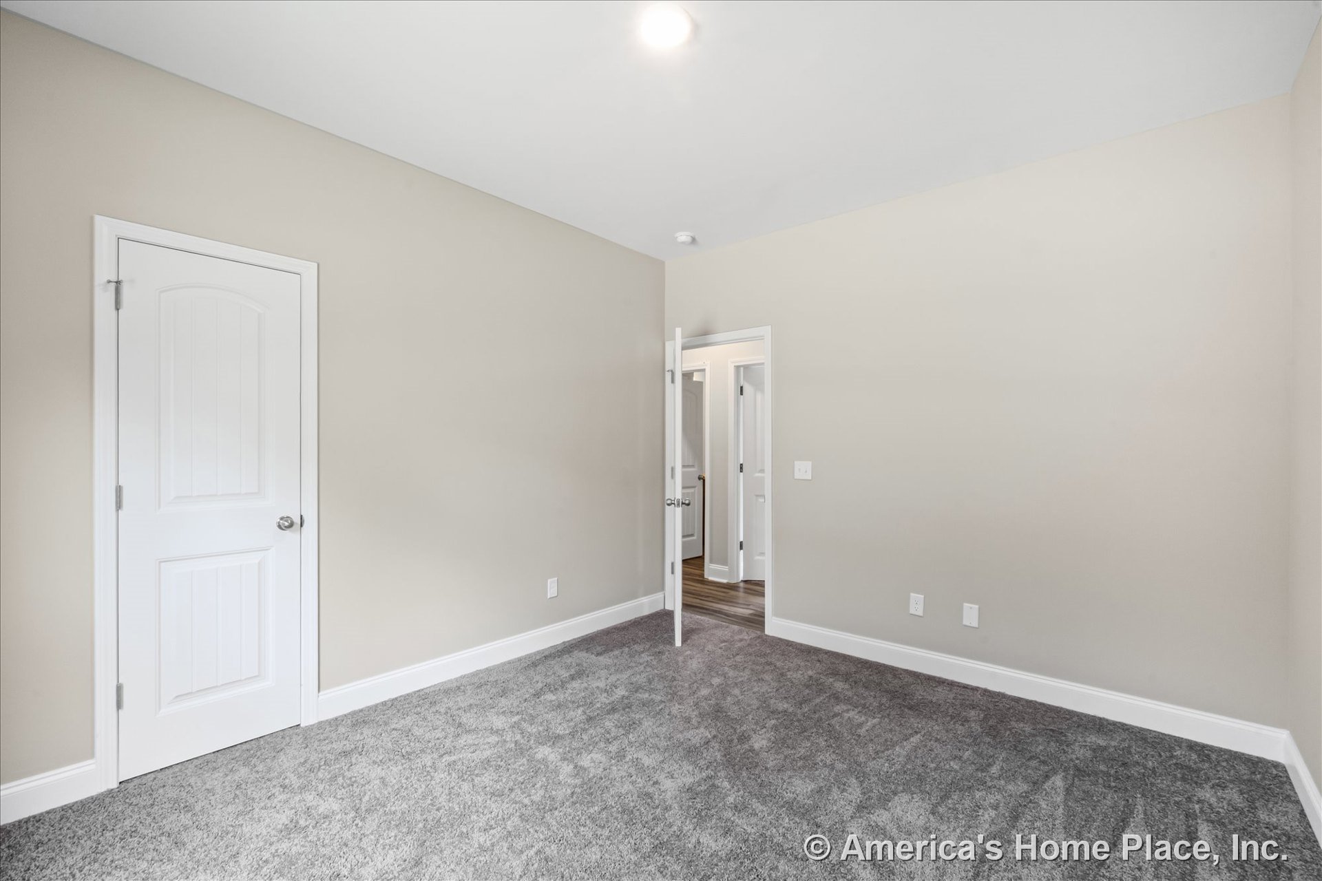 Bedroom with light beige painted walls, white baseboards and trim, gray carpet flooring, white paneled door, recessed ceiling light, and interior doorway.