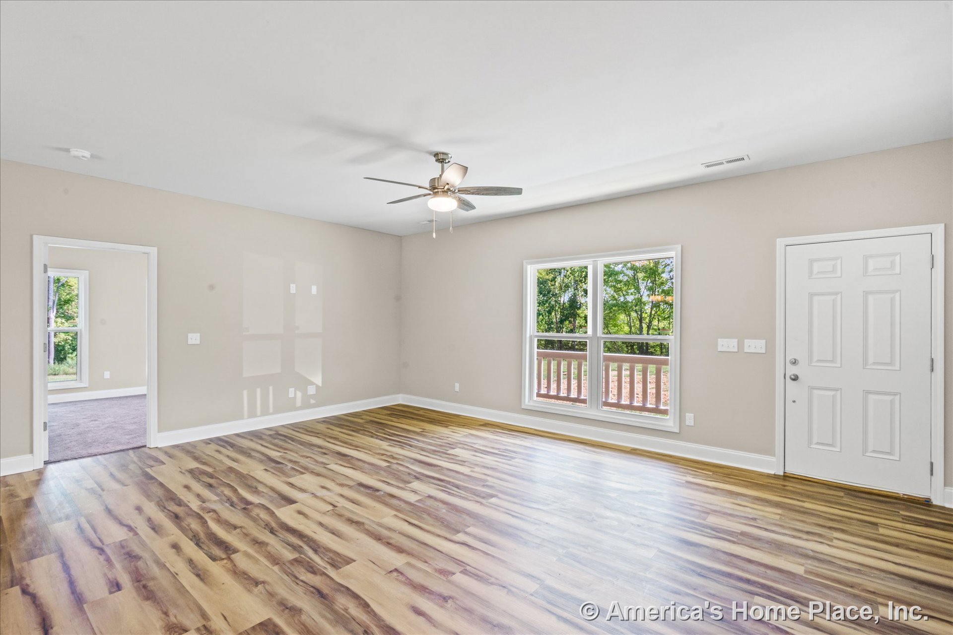 Living room with wood-look vinyl plank flooring, ceiling fan with integrated light, double window with white trim providing porch view, neutral wall paint, white entry door, and