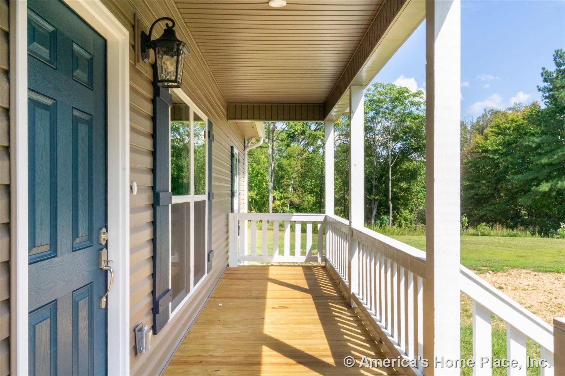 Covered front porch with wood plank flooring, white railings, blue paneled entry door, mounted lantern light fixture, double window with white shutters, and crisp exterior trim and