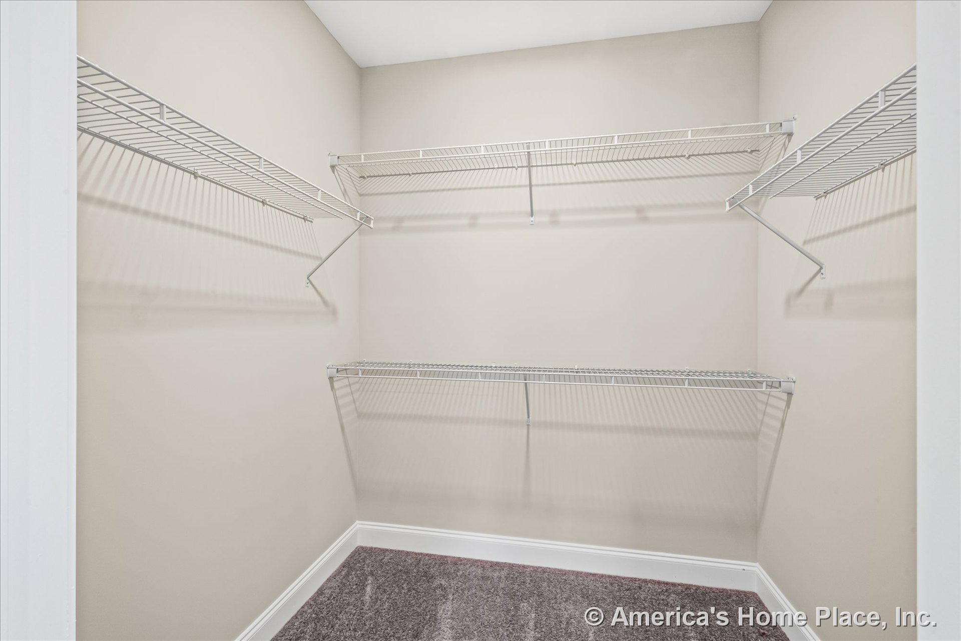 Walk-in closet with multiple white wire shelving units, beige painted walls, carpet flooring, white baseboard trim, and open storage space for organization.