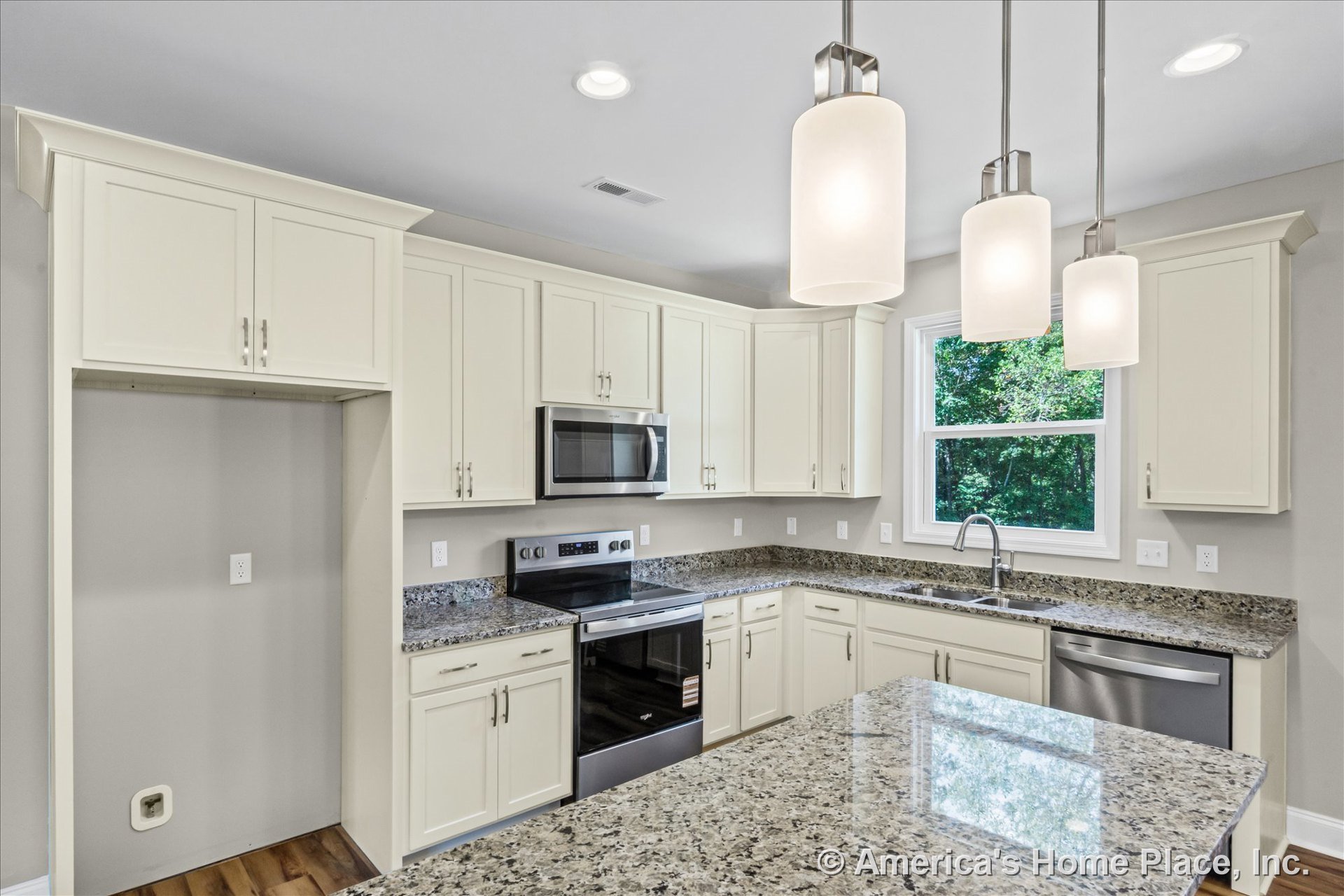 Cream upper and lower cabinets with granite island and perimeter countertops, stainless steel oven and microwave, built-in dishwasher under counter, pendant and recessed ceiling