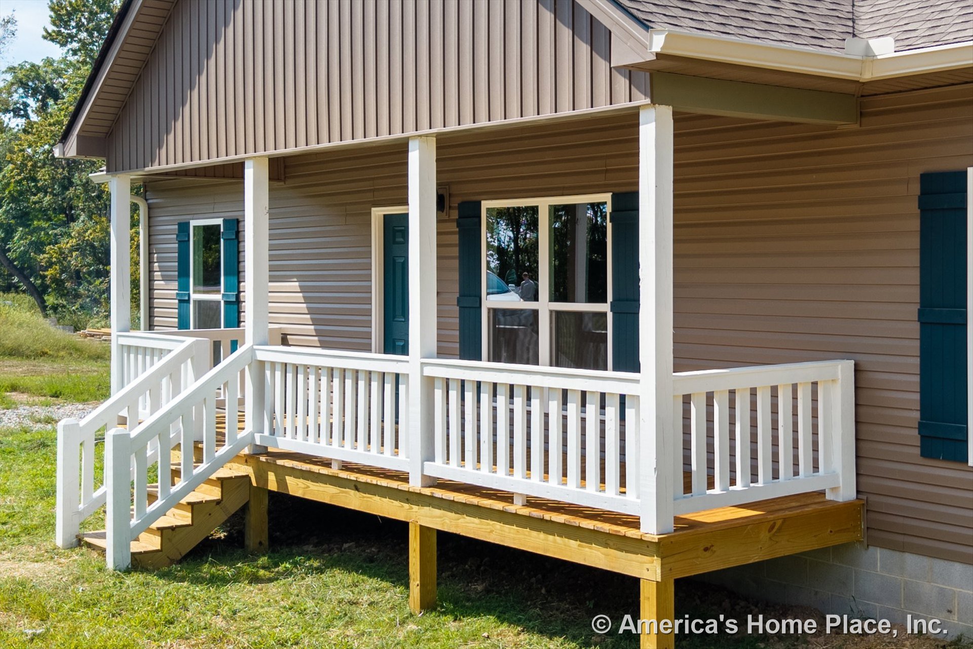 Covered front porch with white railings and wooden floor, tan vinyl siding exterior, blue window shutters, exterior staircase leading to entry, and detailed trim around windows and