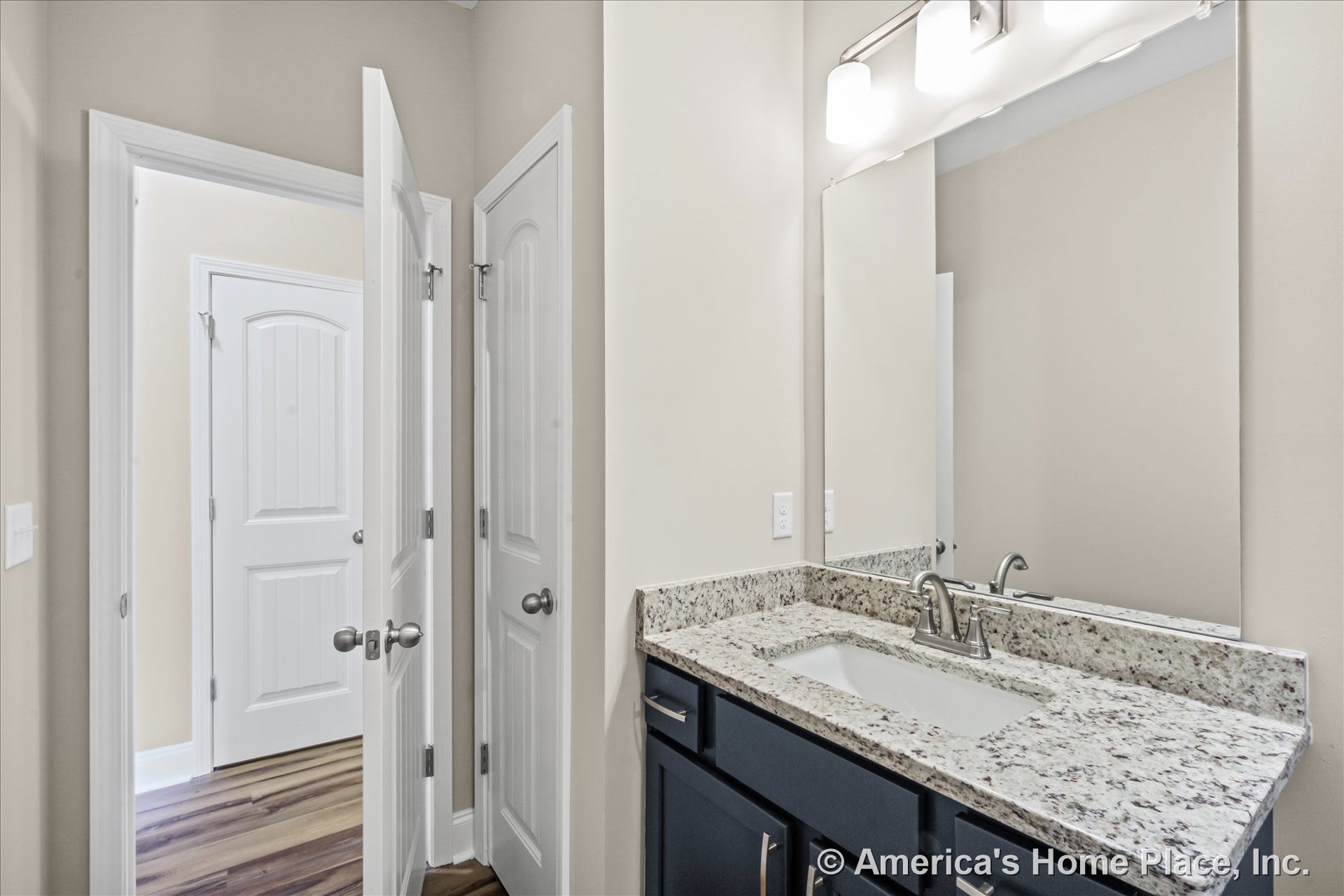 Granite vanity with undermount sink, dark wood cabinets, large wall mirror, three-light fixture above, white paneled doors, painted walls, and tile flooring.