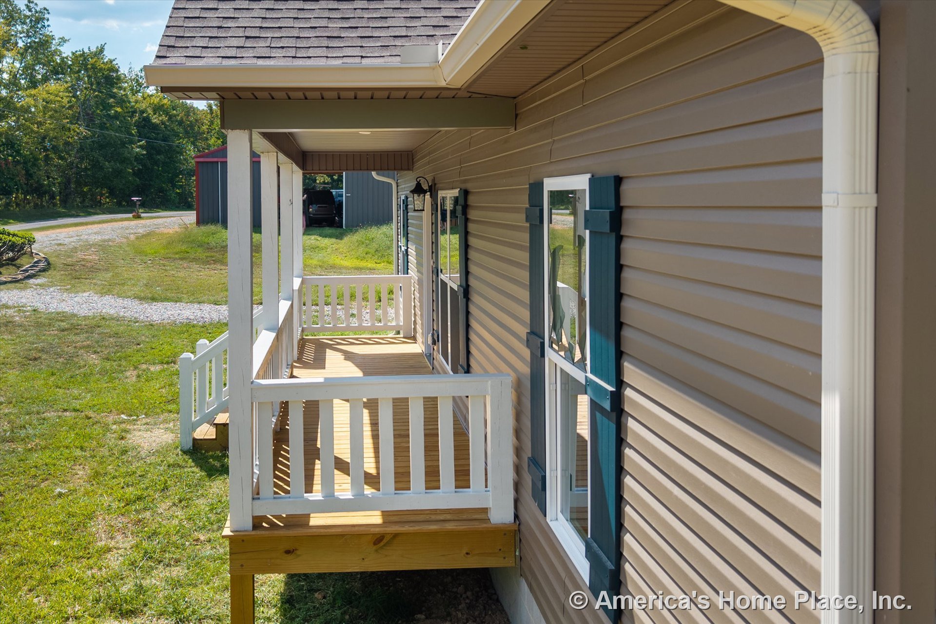 Covered front porch with white railings, wood decking, vinyl siding exterior, blue window shutters, and a gutter system along the roofline.