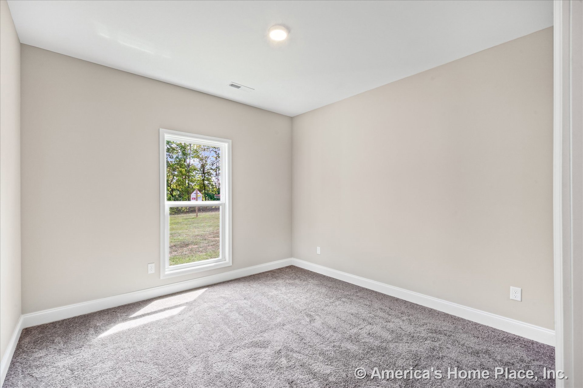 Bedroom with single large window framed in white trim, neutral beige walls, gray carpet flooring, white baseboards, recessed ceiling light, and rectangular room layout.