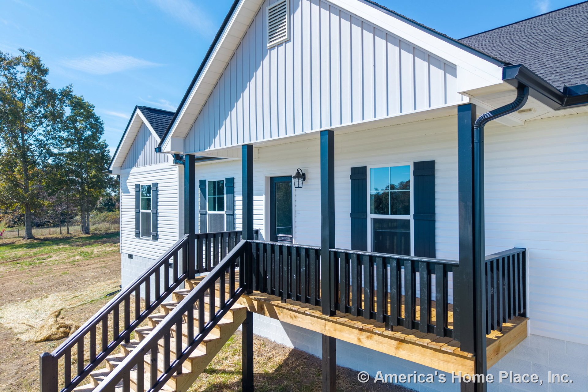 Covered front porch with black vertical railings, white horizontal siding, double-hung windows with shutters, exterior wall-mounted light fixture, gable roof with asphalt shingles