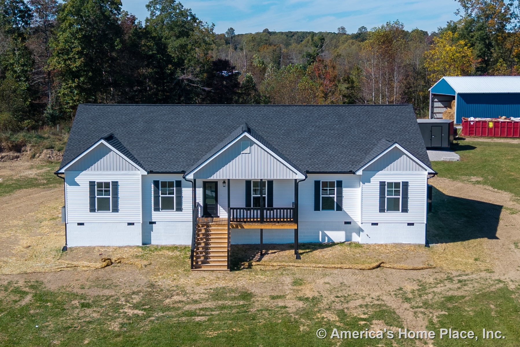 Covered front porch with wooden steps and railings, white vinyl siding, black shingle roof, multiple double-hung windows, and contrasting trim accents.