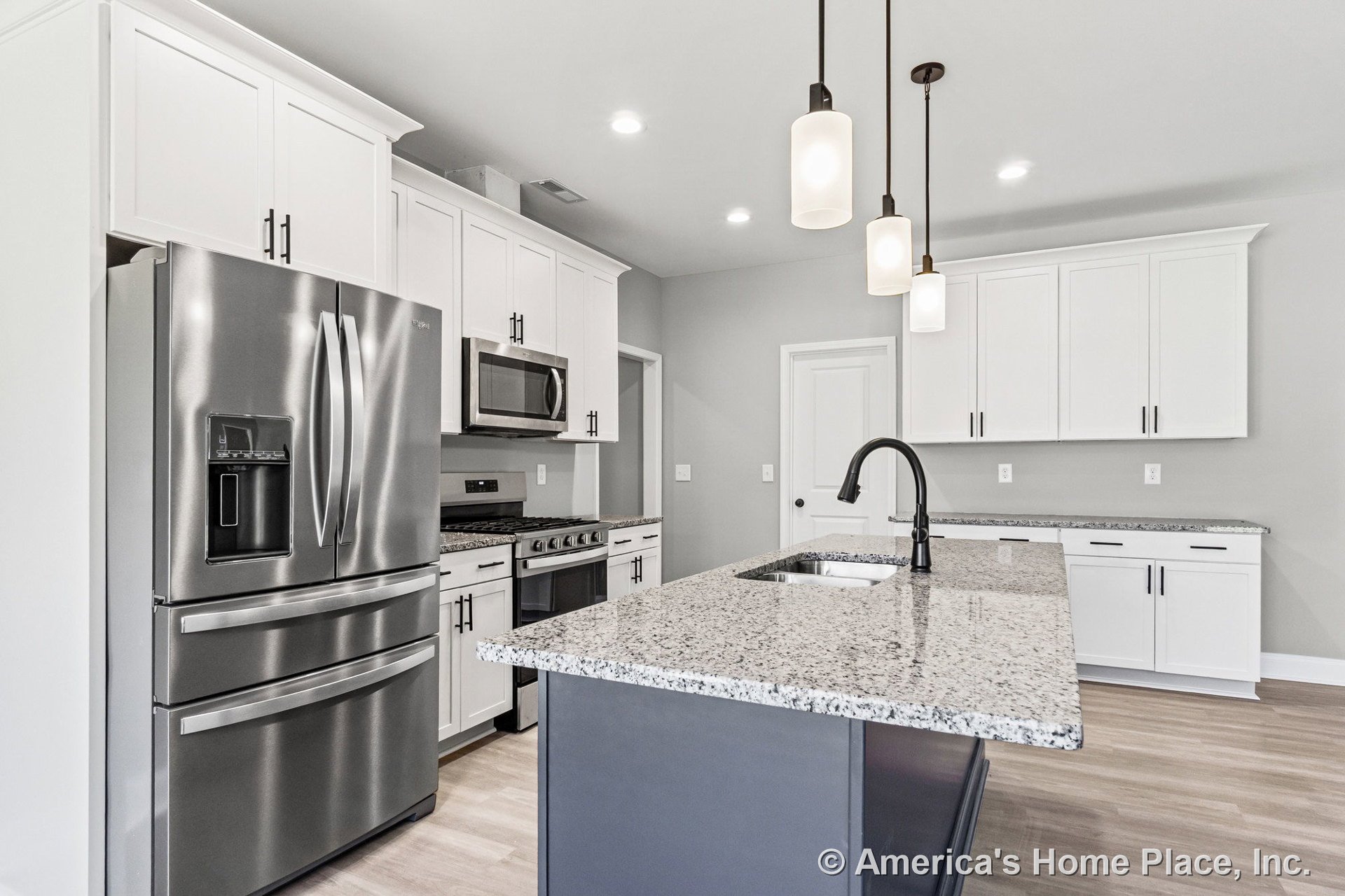 Granite island with undermount sink and modern faucet, surrounded by white shaker cabinets, stainless steel French door refrigerator, built-in microwave above gas range, pendant