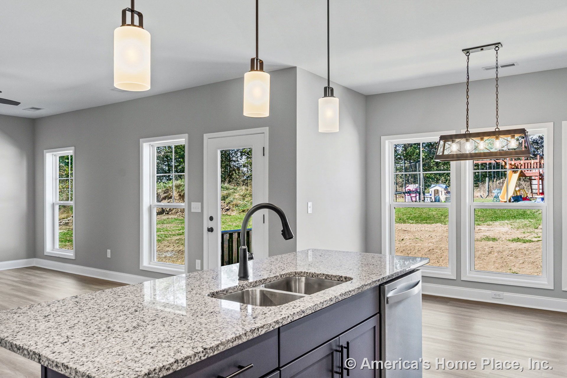 Granite island countertop with undermount double sink and modern pendant lights, light wood flooring, gray painted walls, open layout with large windows, white cabinetry, and