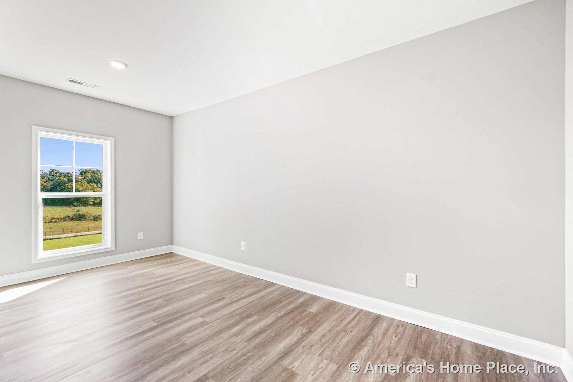 Large window with white casing, recessed ceiling light, light gray painted walls, wood-look vinyl plank flooring, white baseboards, single electrical outlet.