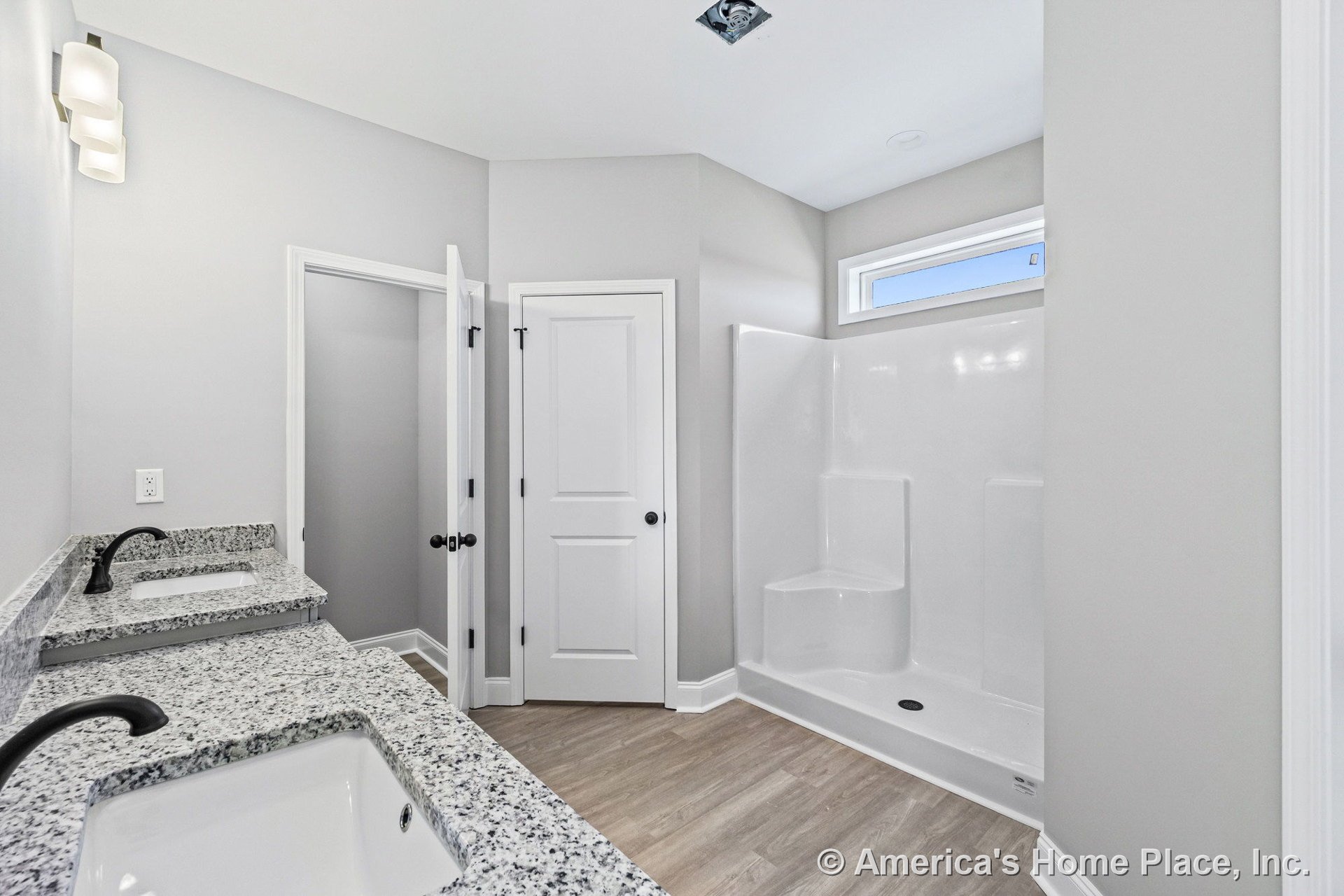 Double vanity with granite countertops and matte black faucets, white shaker cabinet doors, walk-in shower with built-in seat and window above, modern wall sconce lighting