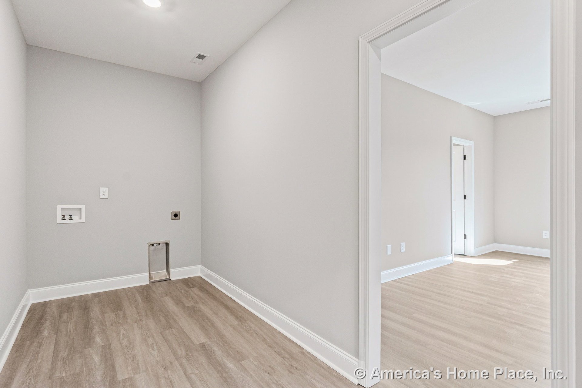 Laundry room with utility hookups, light wood-look vinyl plank flooring, white baseboards and trim, recessed ceiling light, neutral wall color, and open doorway leading to an